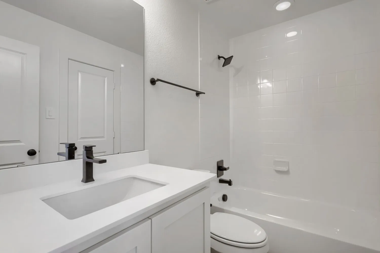 White vanity with an integrated sink, matte black faucet, and frameless mirror