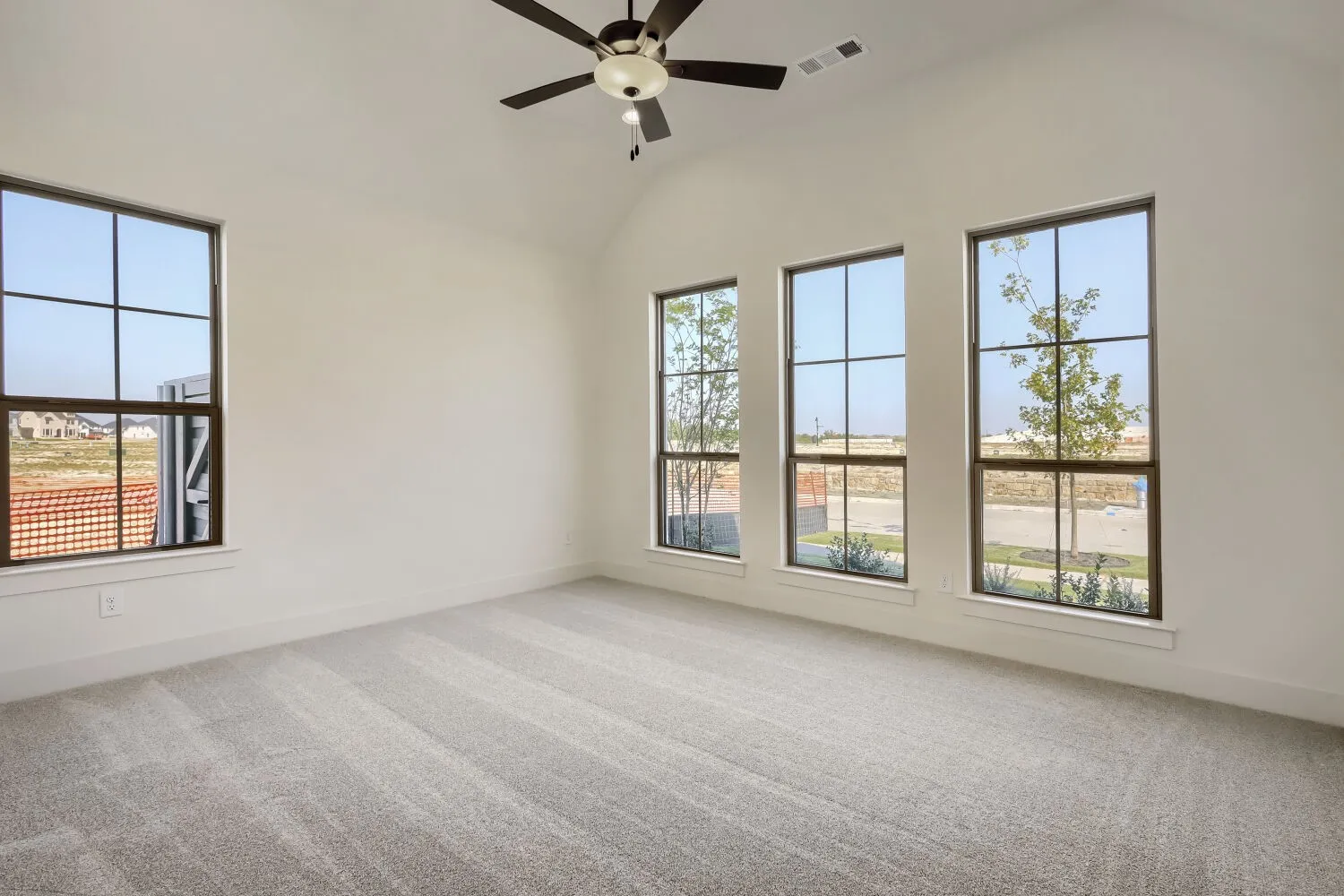 Vaulted ceiling with a ceiling fan, light gray carpeting, and multiple windows with dark trim