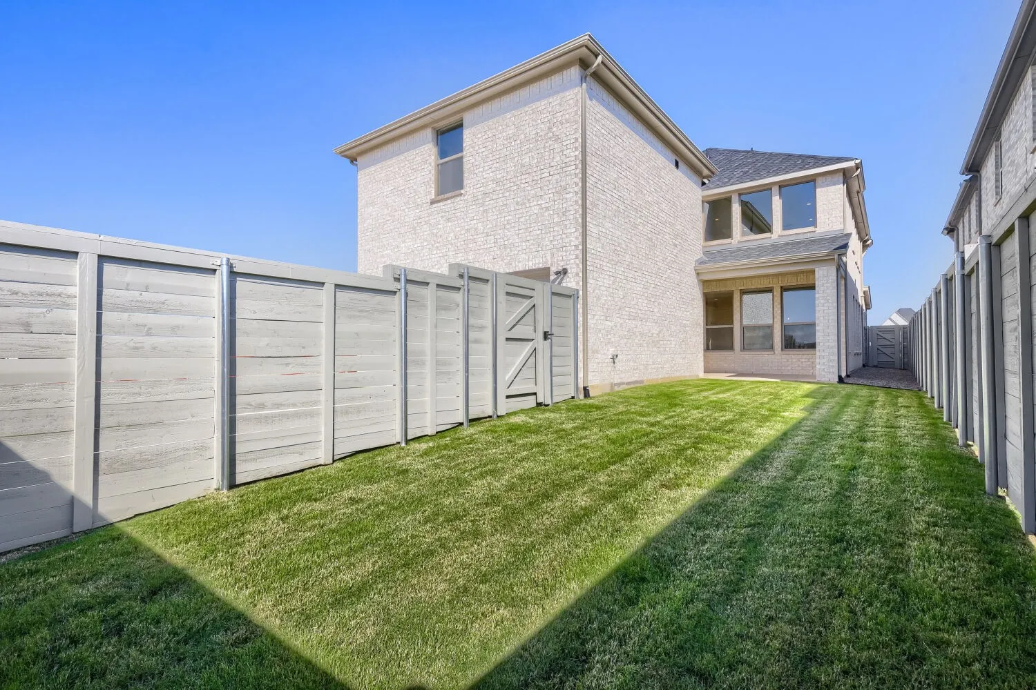 Spacious backyard featuring a manicured lawn with mature landscaping, bordered by composite fencing