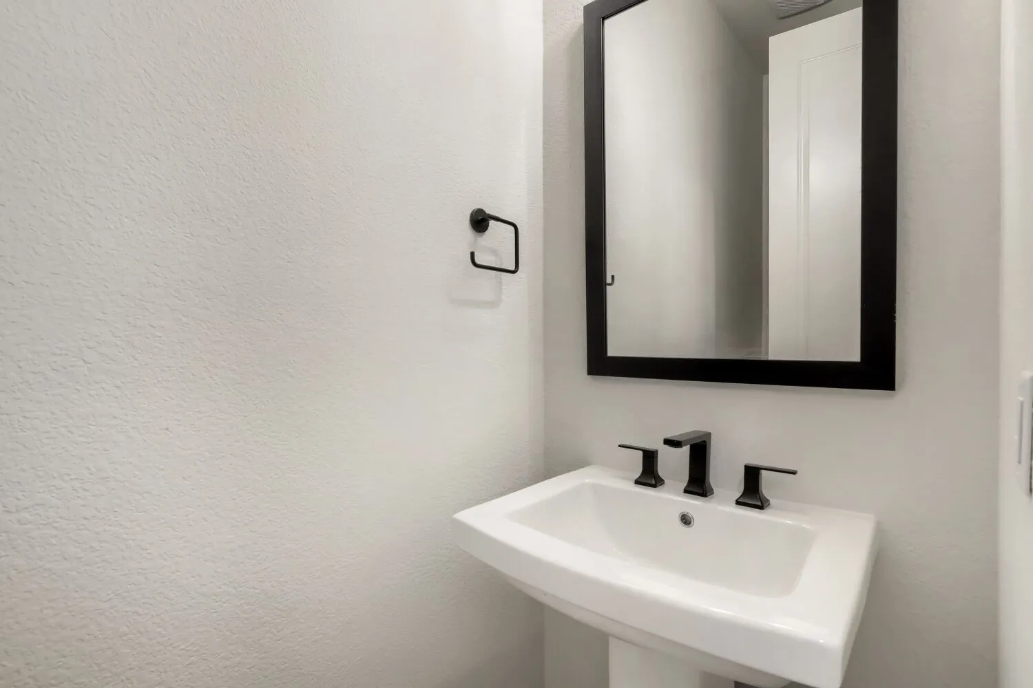 Pedestal sink with a rectangular basin, matte black faucet, and a wall-mounted framed mirror