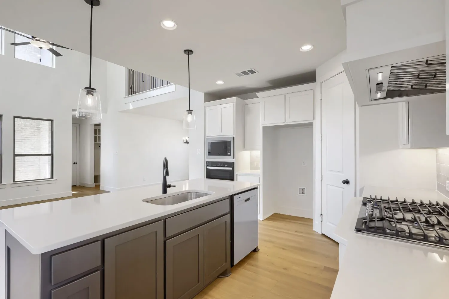 Open-concept kitchen featuring light wood-finish flooring, a center island with sink and storage, built-in stainless steel appliances, and abundant white cabinetry