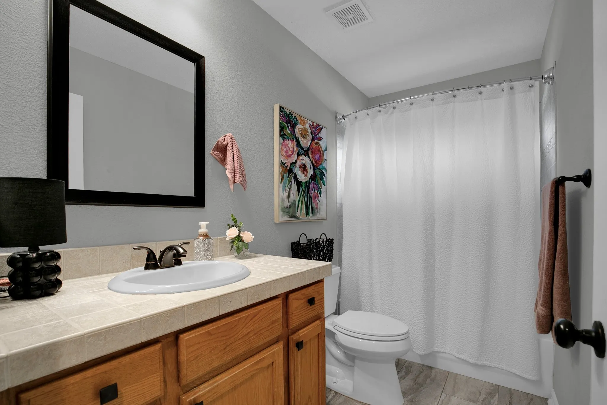 Vanity with wood-finish cabinetry, tile countertop, and an undermount sink