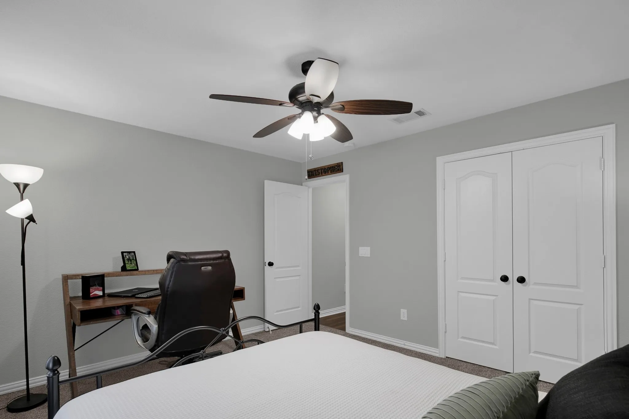 Ceiling fan with light fixture, light gray wall paint, white trim, white paneled doors with black hardware, and carpet flooring