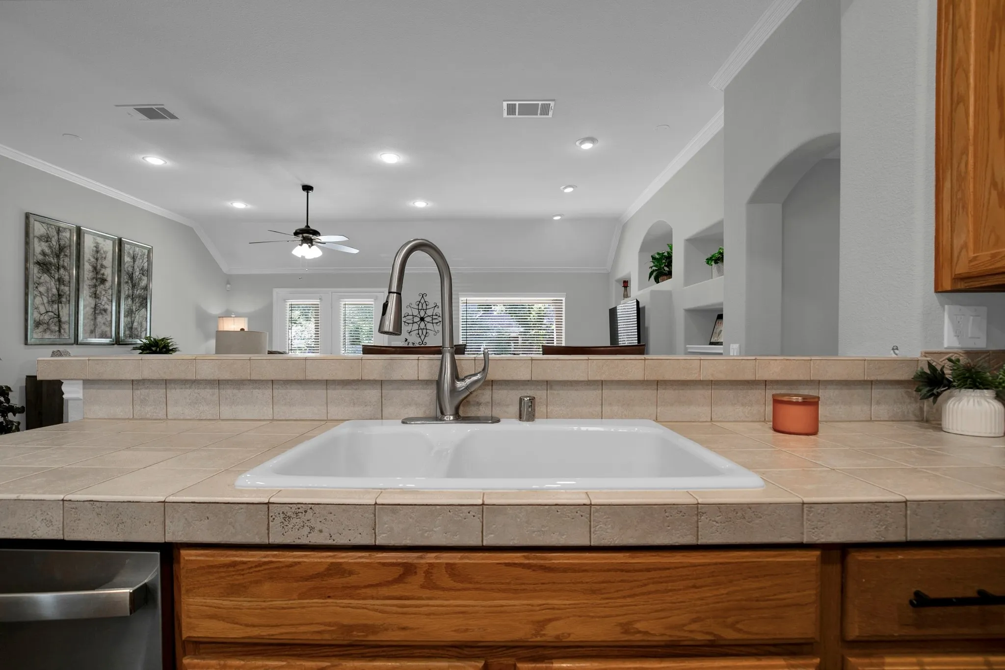 Kitchen sink with a high-arc faucet, tile countertops, wood cabinetry, and recessed lighting