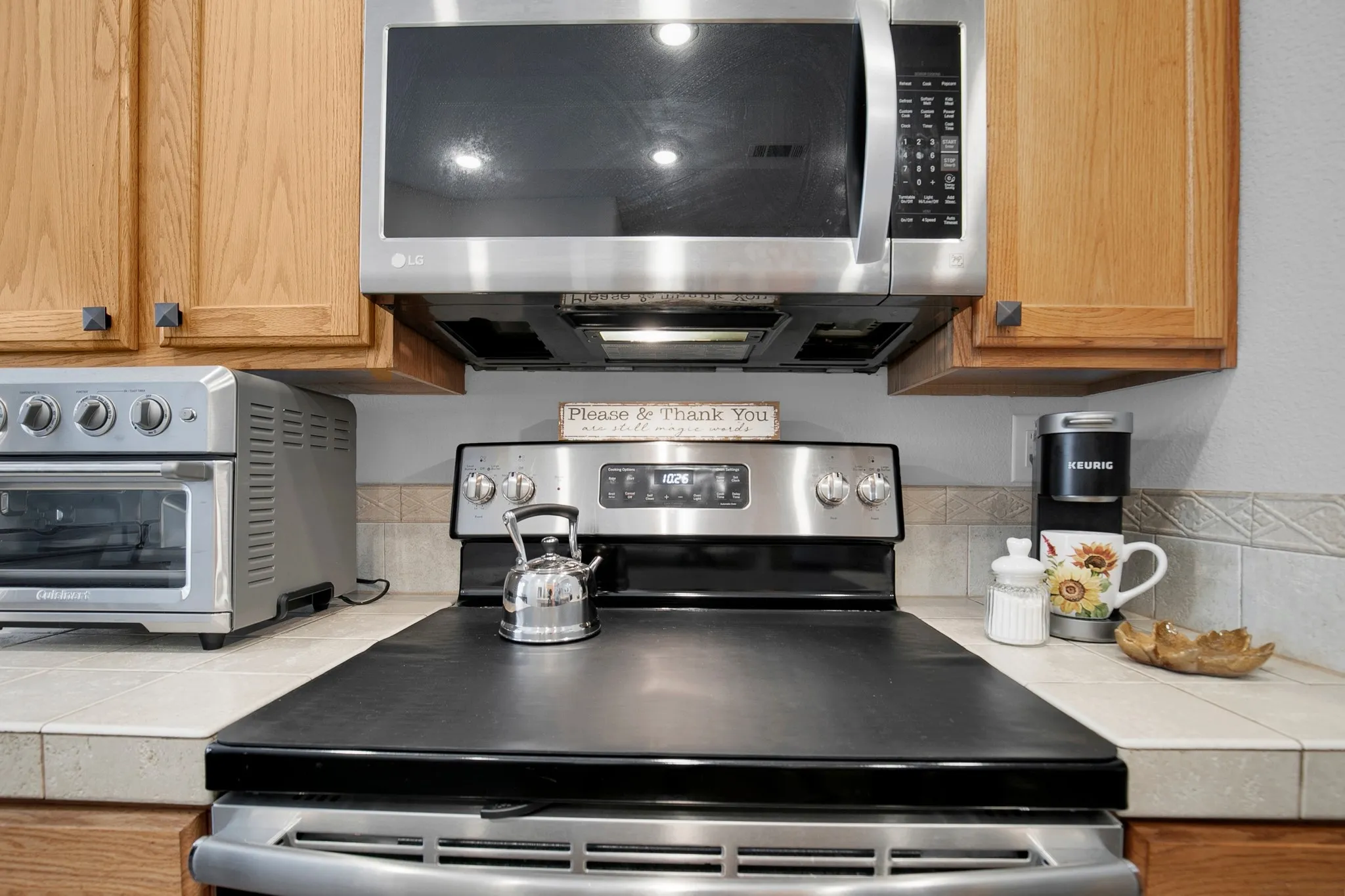 Stainless steel range with a built-in microwave, light wood cabinetry, and a light-toned tile backsplash