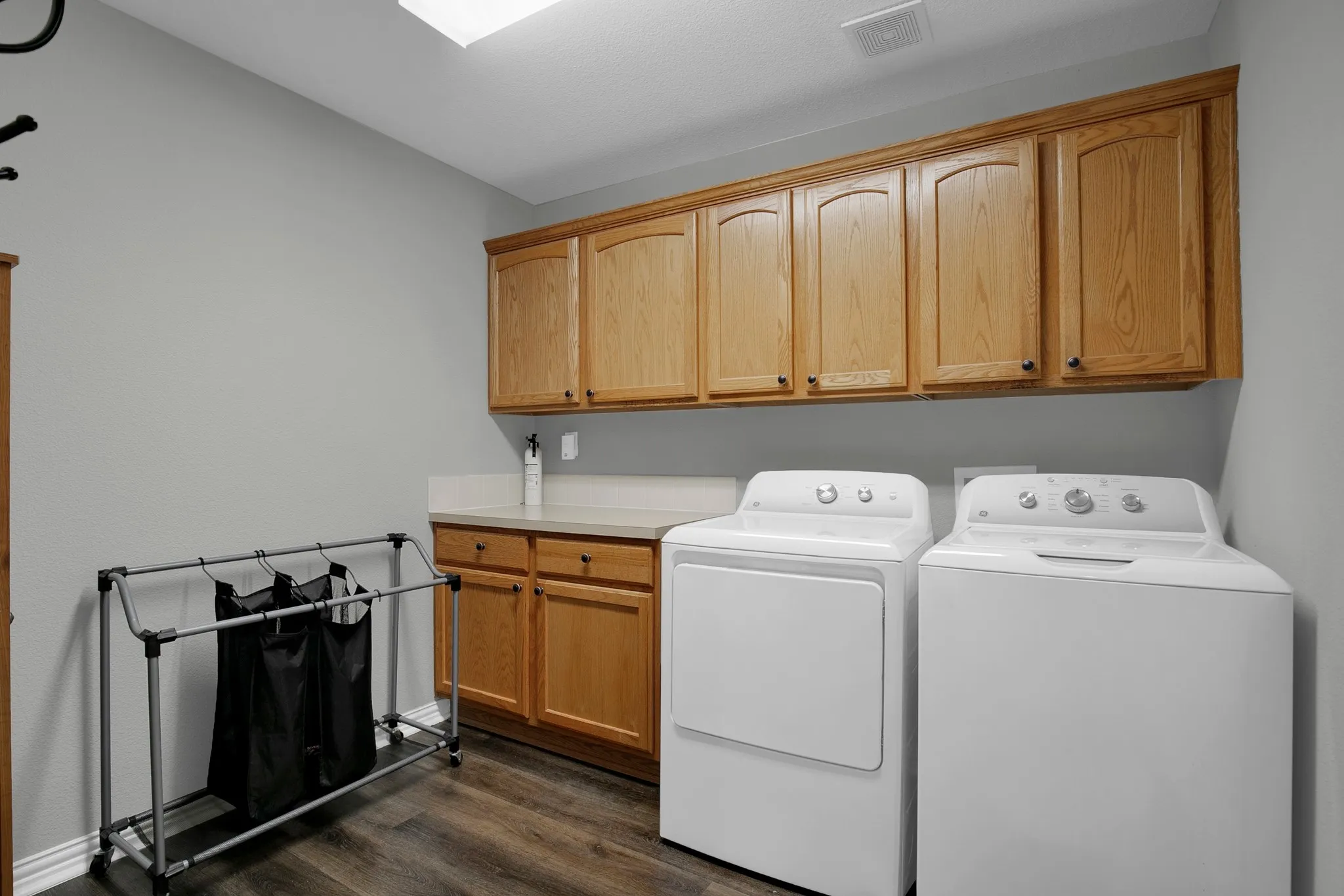 Laundry area with wood-finish flooring, light wood cabinetry, and a light-toned countertop