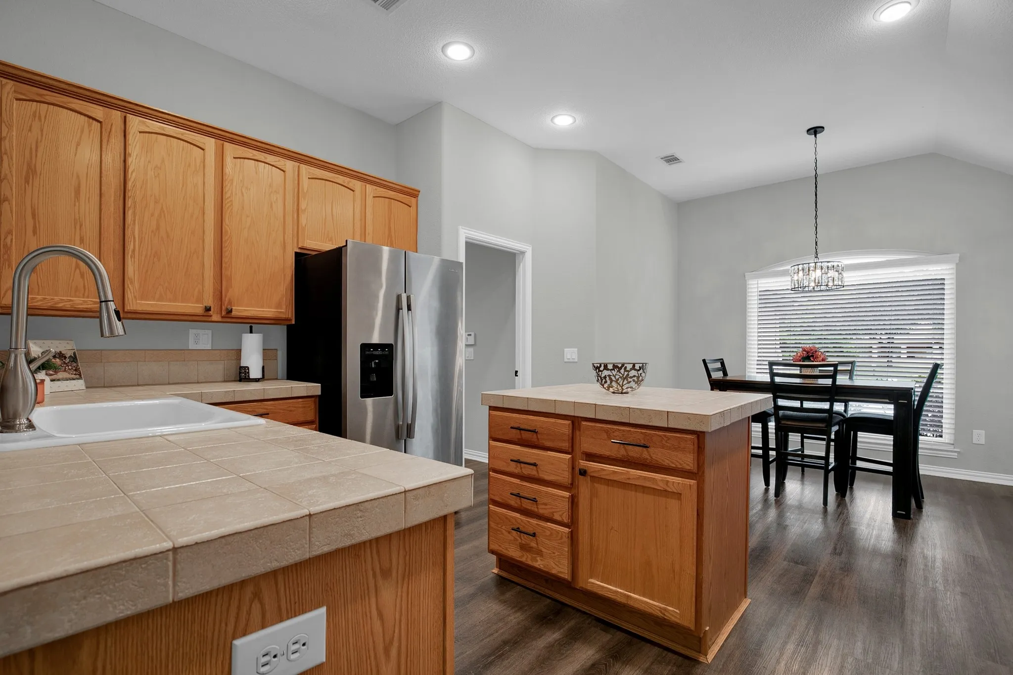 Kitchen featuring wood cabinetry, tile countertops, an undermount sink, stainless steel appliances, and wood-finish flooring