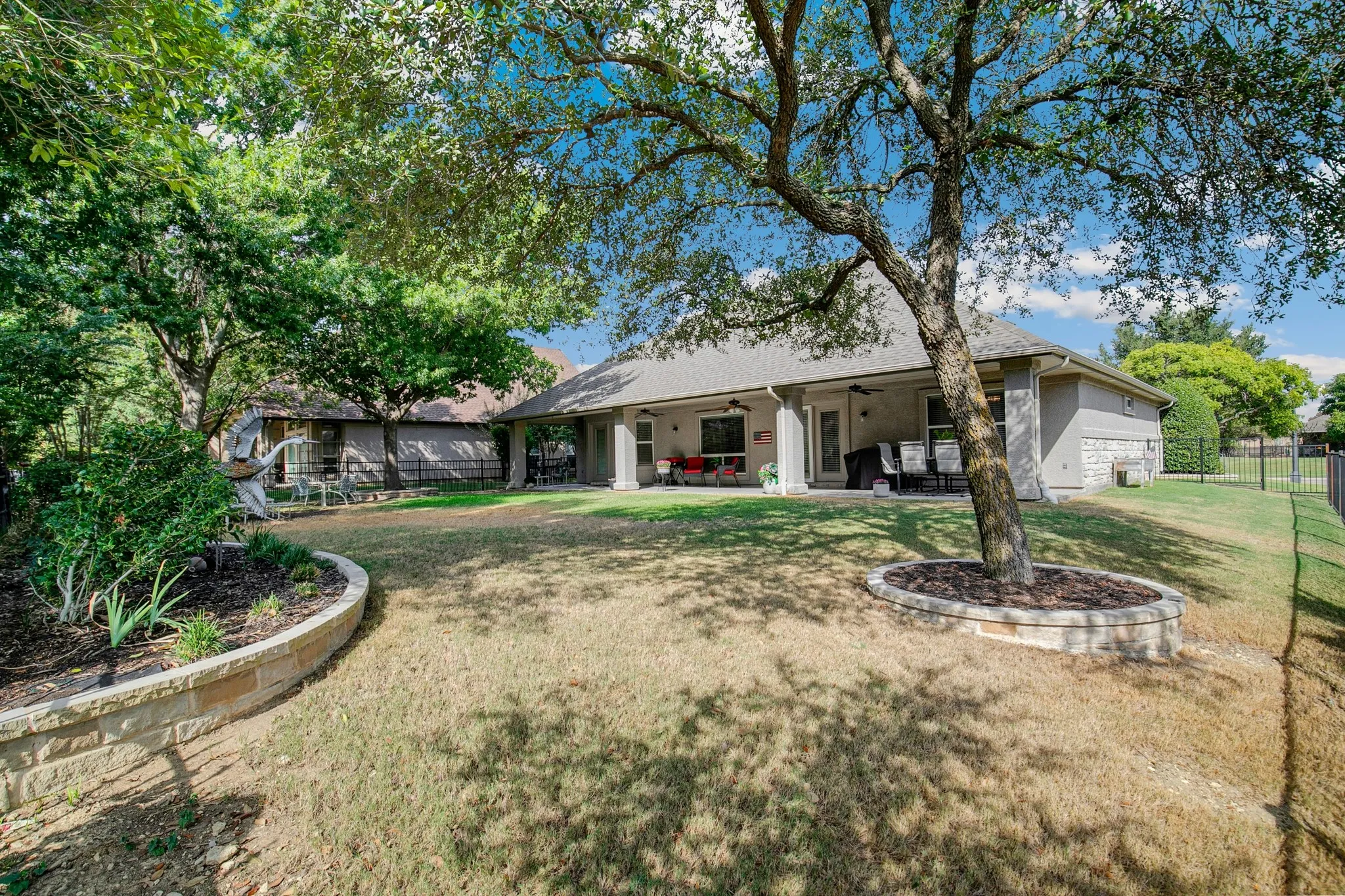 Expansive backyard with a covered patio, a stone retaining wall, and mature trees