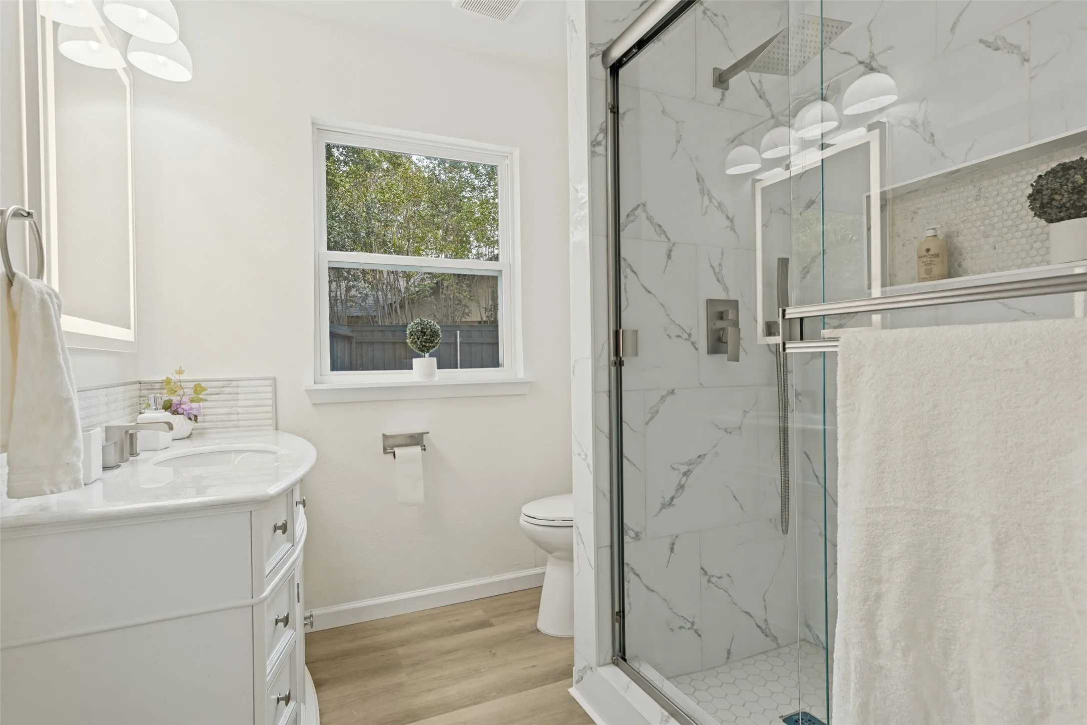 Contemporary bathroom featuring a glass-enclosed shower with large format tile and a hexagon tile floor, a white vanity with an integrated sink, and wood-finish flooring