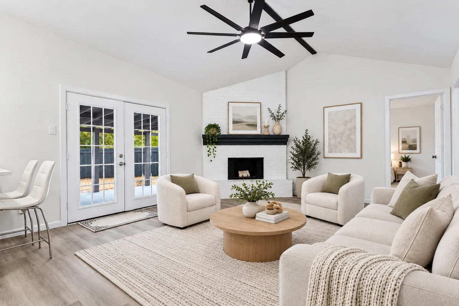 Vaulted ceilings, wood-finish flooring, white brick fireplace with a black mantel, and double French doors with grid-patterned glass