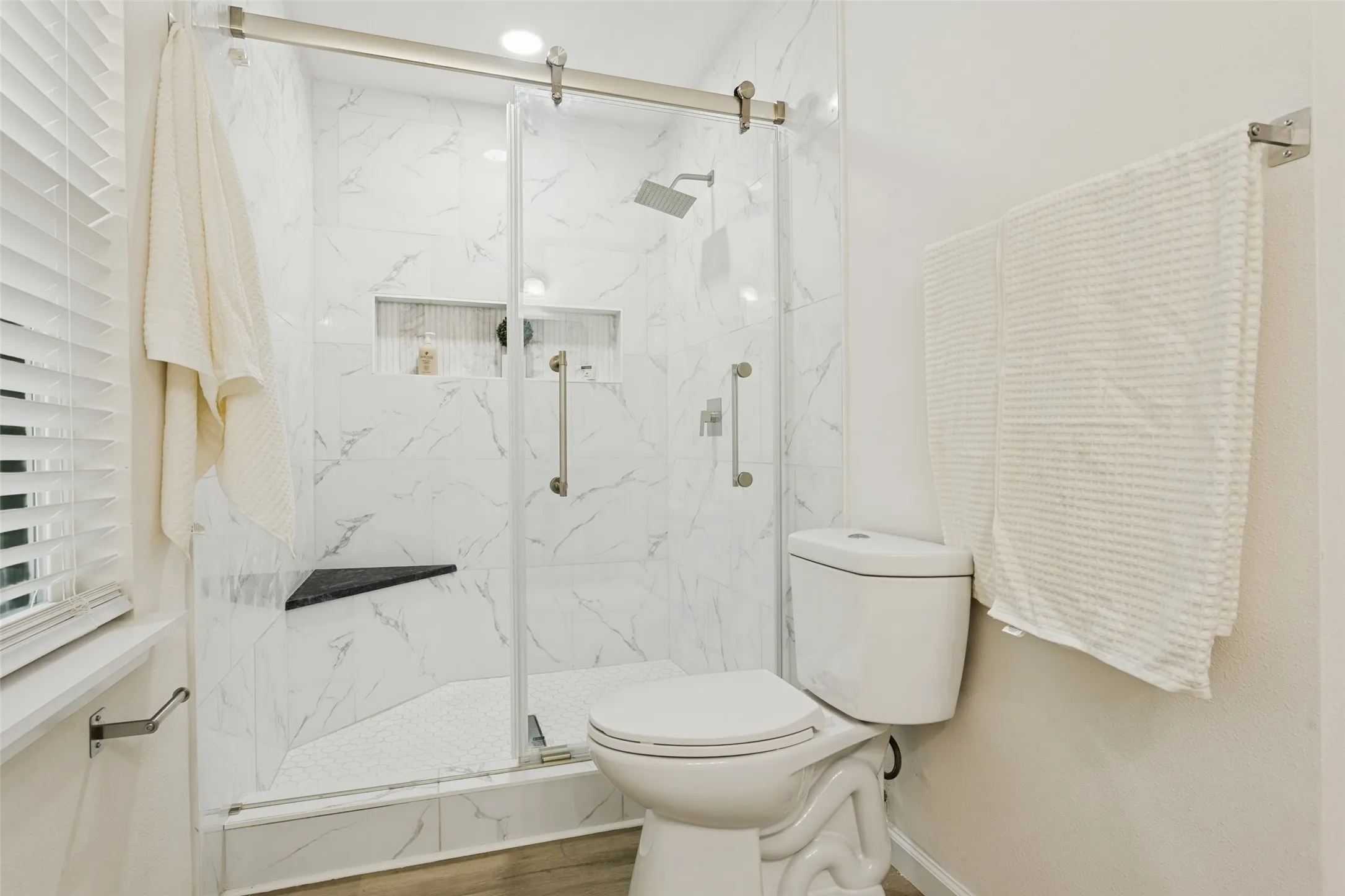 Glass-enclosed shower with white marble-patterned tile, integrated shower bench, and recessed shelving