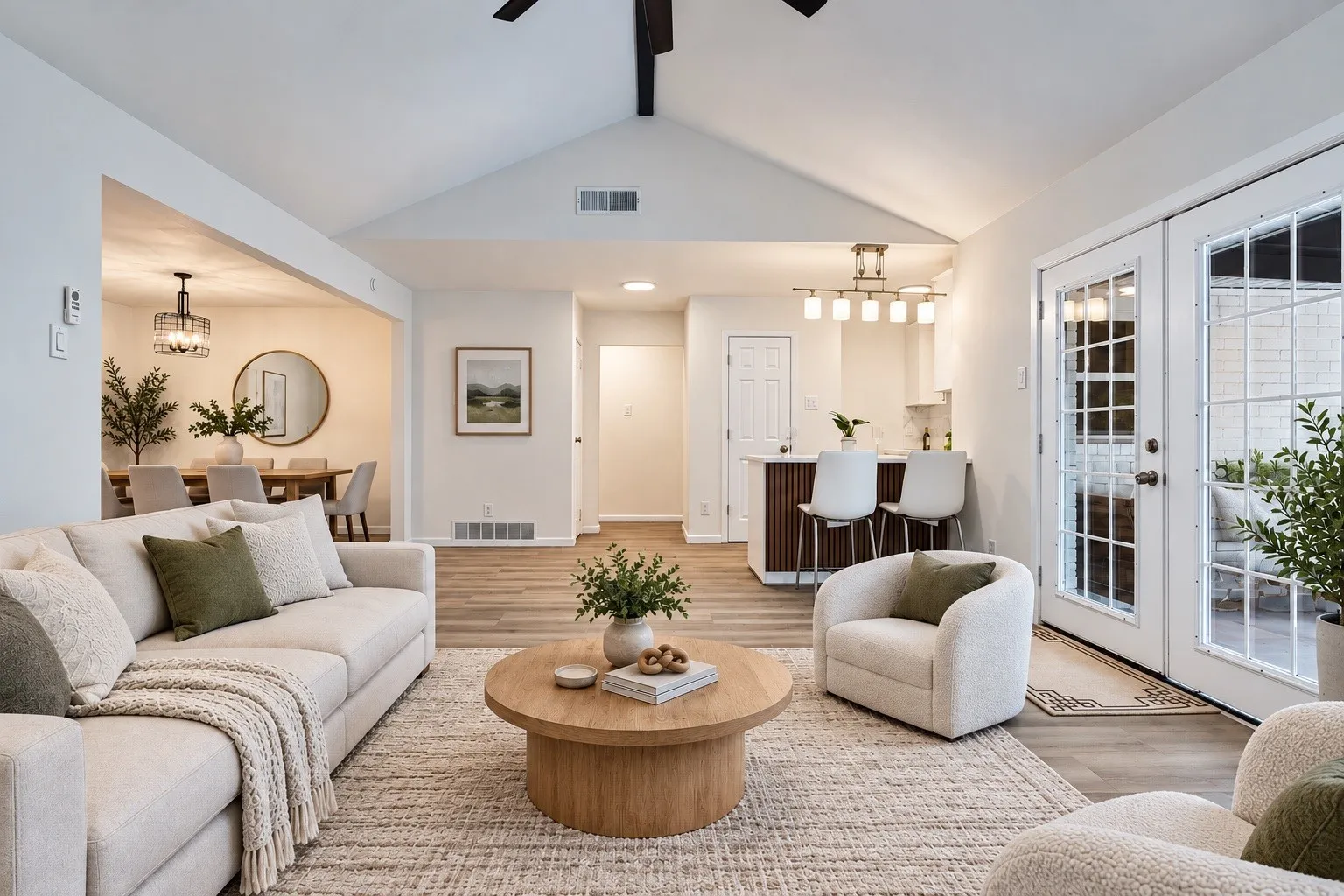 Vaulted ceiling, wood-finish flooring, white double French doors with grid panes, built-in kitchen bar with seating, recessed lighting