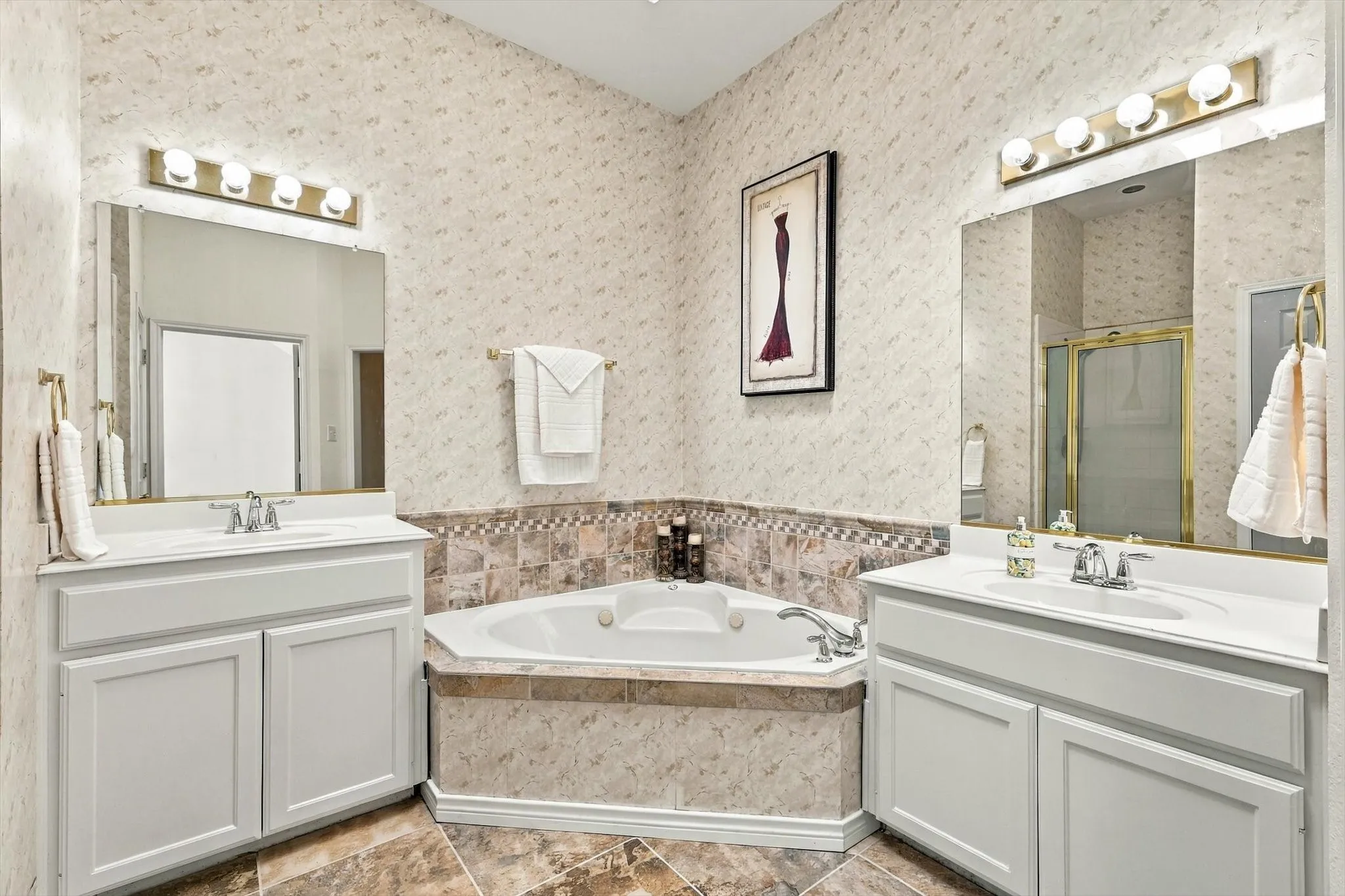 Dual vanities with integrated sinks, corner jetted tub with tile surround, and tile flooring