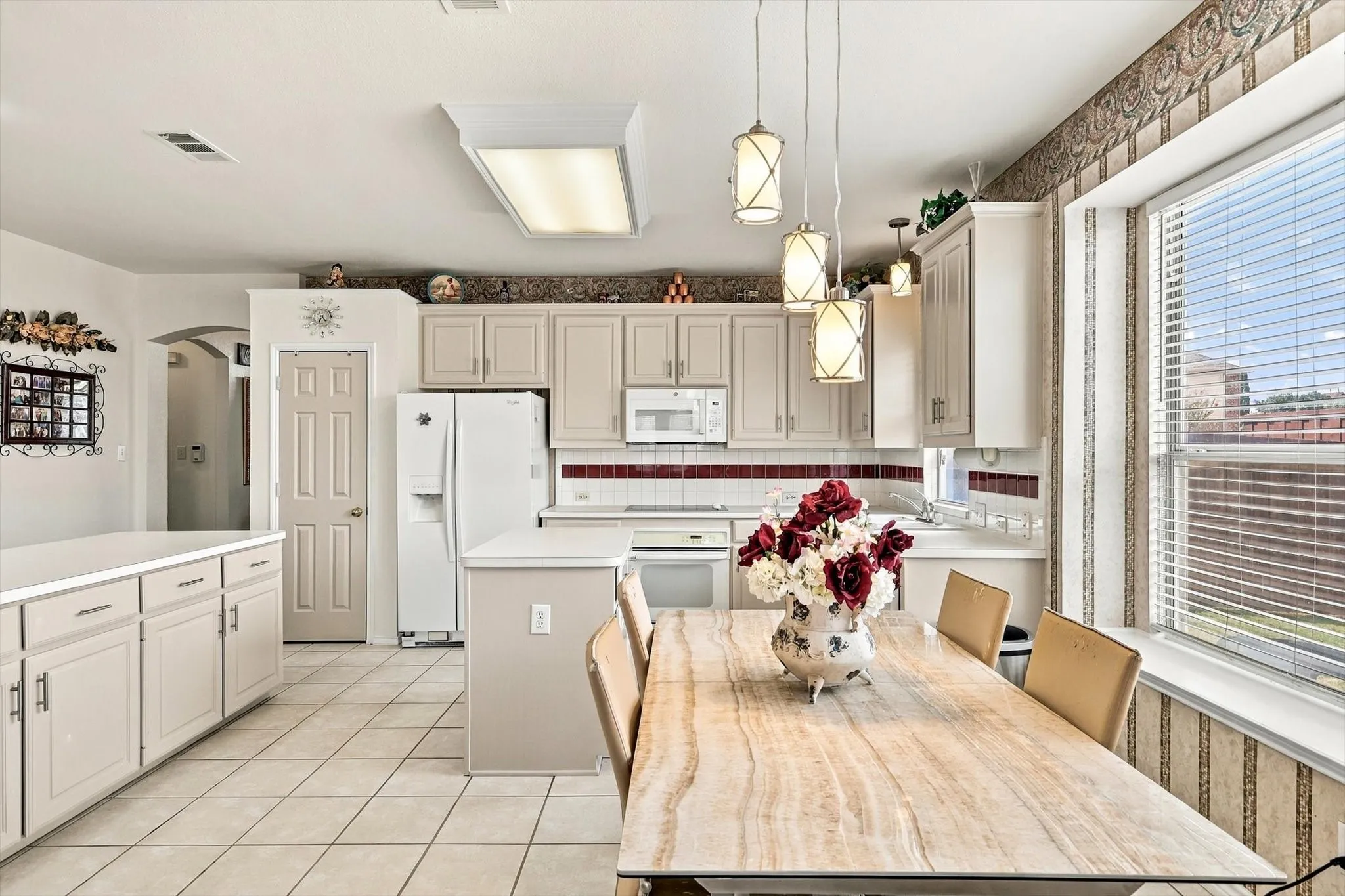 Tile flooring, white cabinetry, white appliances, pendant lighting, and a kitchen island