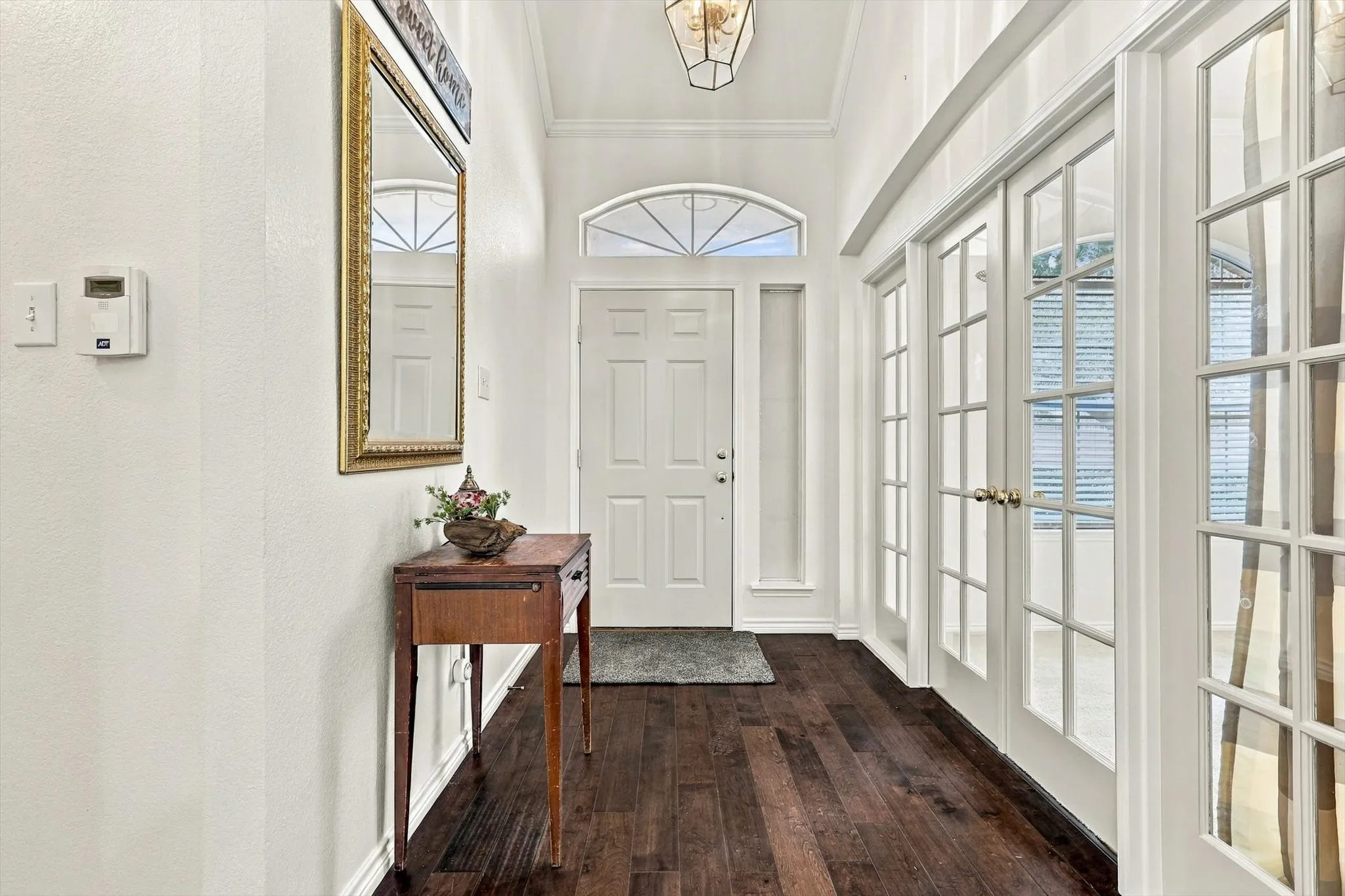 Wood-finish flooring, white paneled walls, a vaulted ceiling, a transom window above the entry door, and double French doors