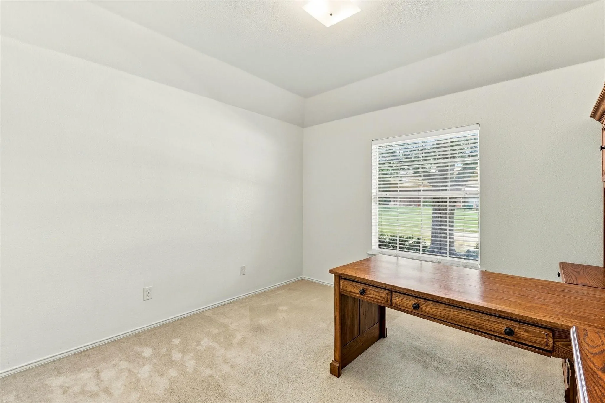 Recessed ceiling with an integrated light fixture, window with horizontal blinds, and carpeting