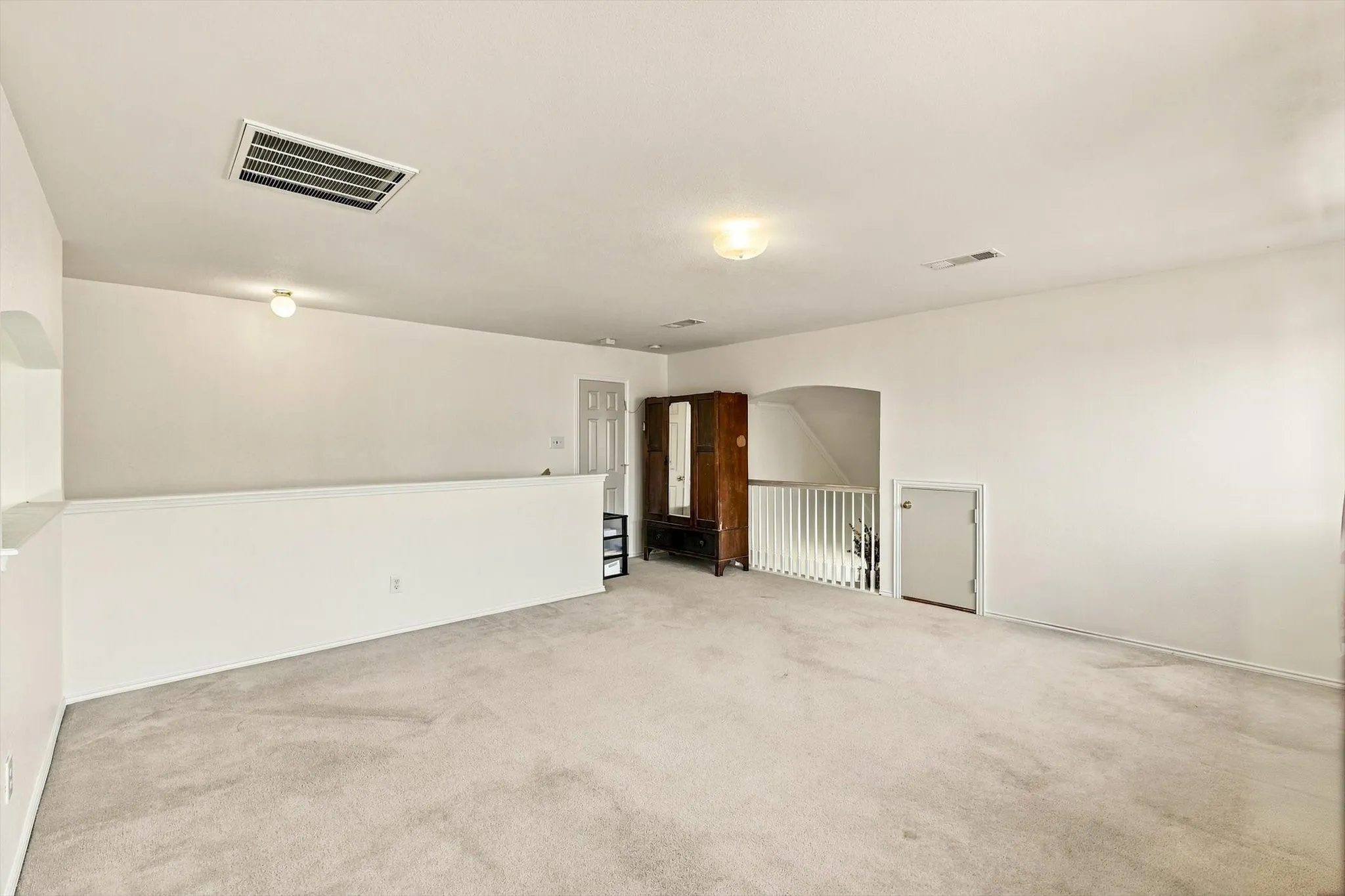 Expansive carpeted area with white walls, recessed ceiling lighting, and a white half-wall railing