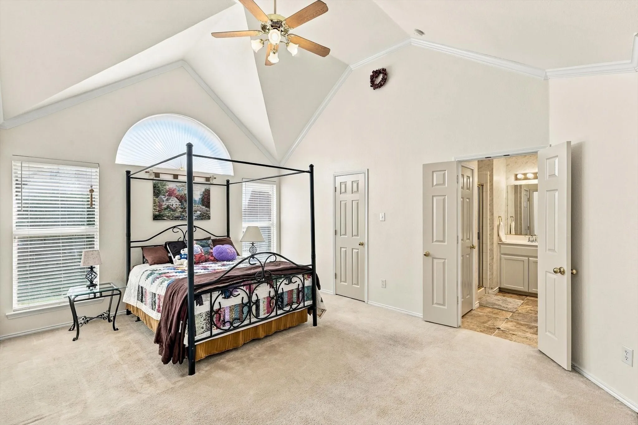 Vaulted ceiling with a ceiling fan, arched window, two additional windows, and beige carpeting