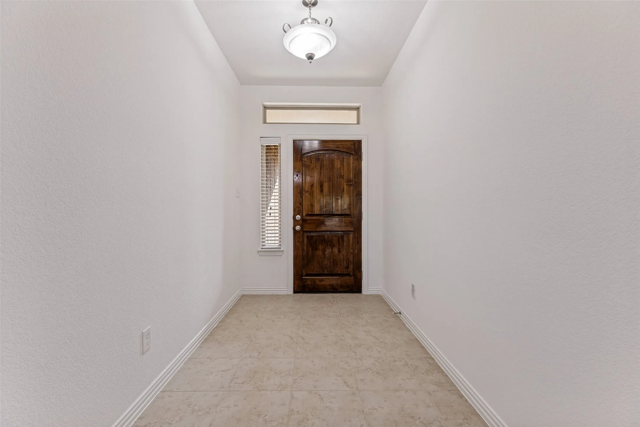 Rich wood-finish entry door, transom window, and tiled flooring