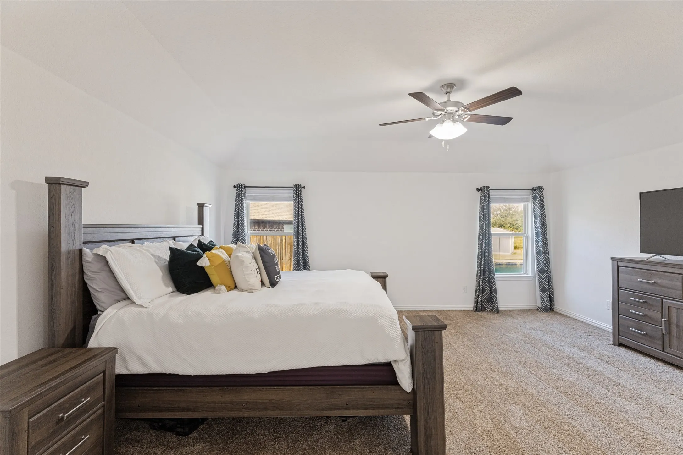 Vaulted ceiling with a ceiling fan, dual windows, and plush carpet flooring