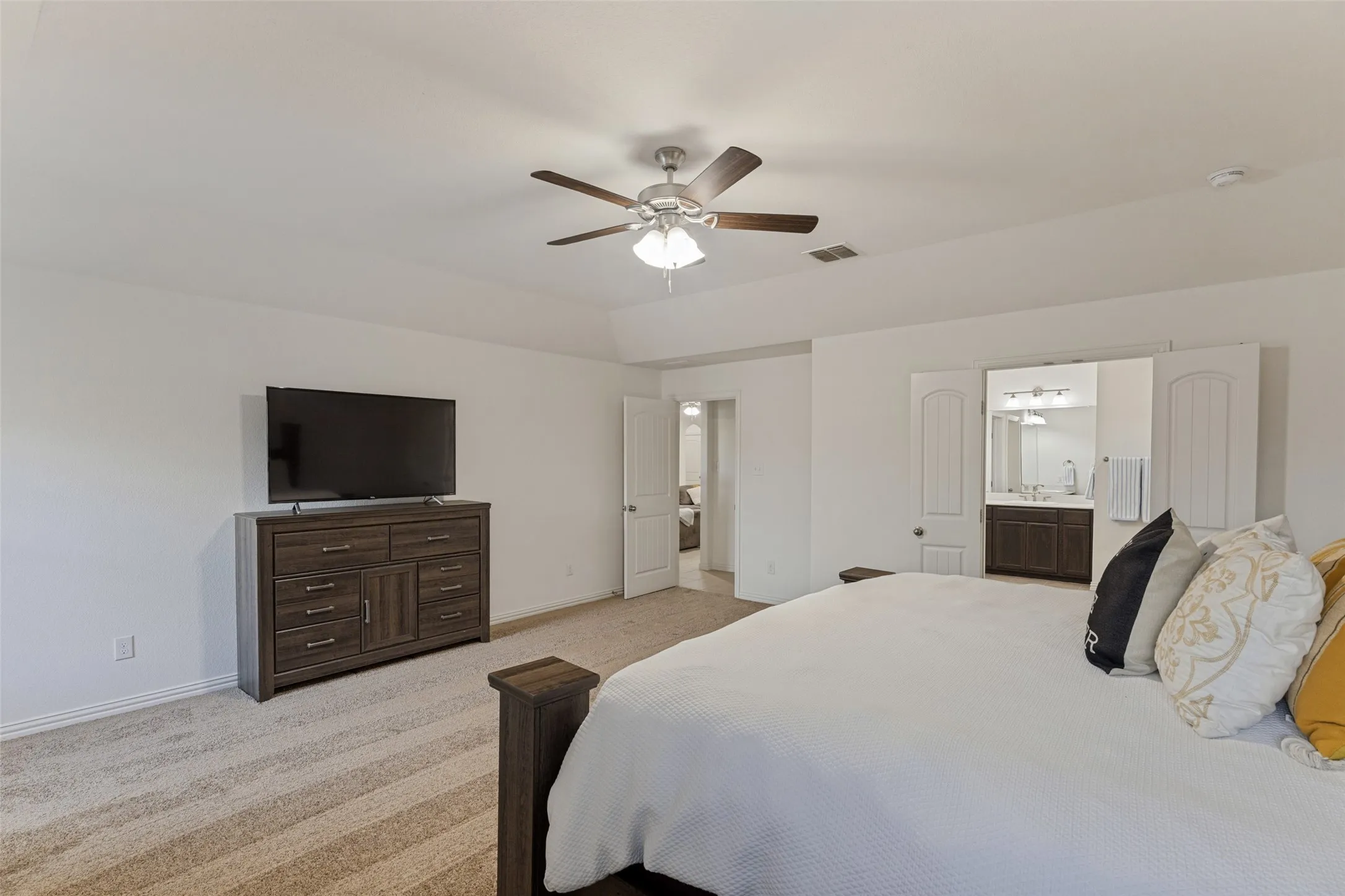 Recessed ceiling with a central fan, carpet flooring, and a barn door entry to a bathroom featuring a vanity with a dark wood-finish cabinet and dual sinks