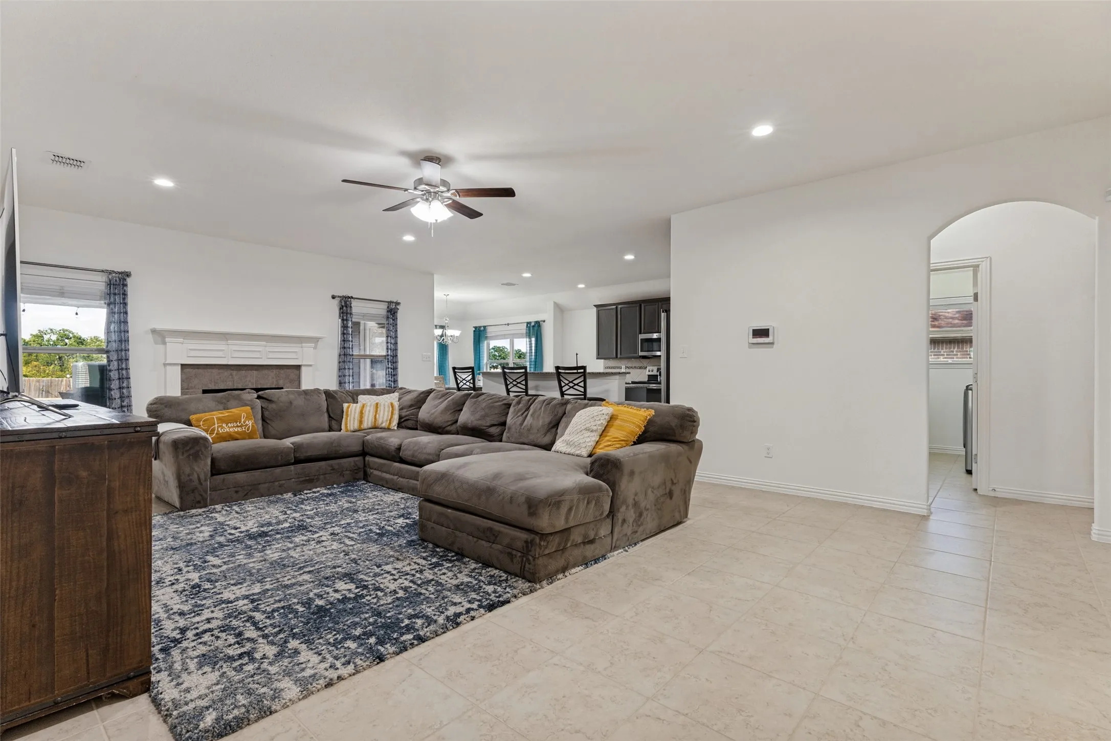 Recessed lighting illuminates the open-concept living space with tile flooring, a fireplace, and a ceiling fan