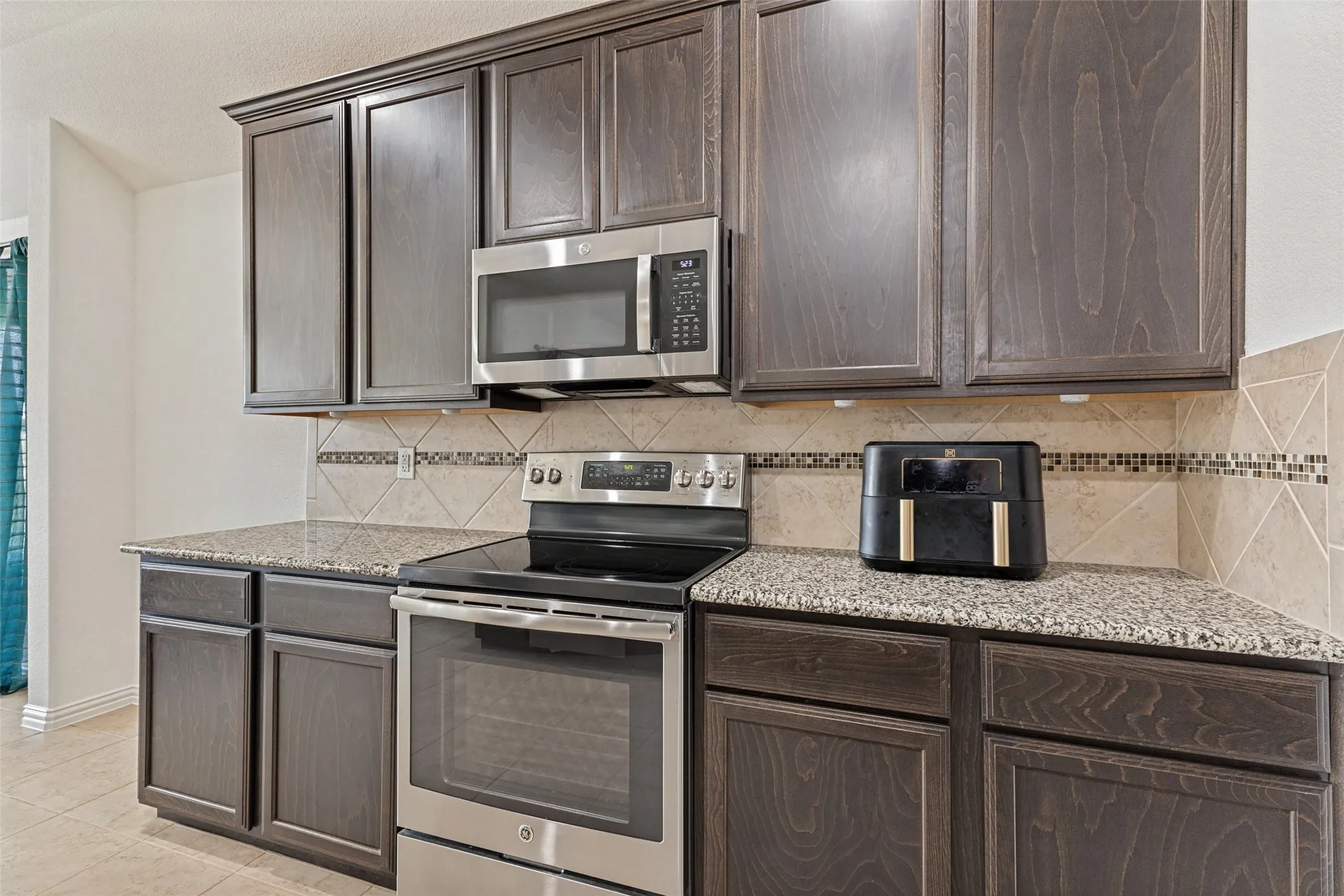 Dark wood-finish cabinetry, speckled countertops, stainless steel appliances, and a tiled backsplash with decorative accents