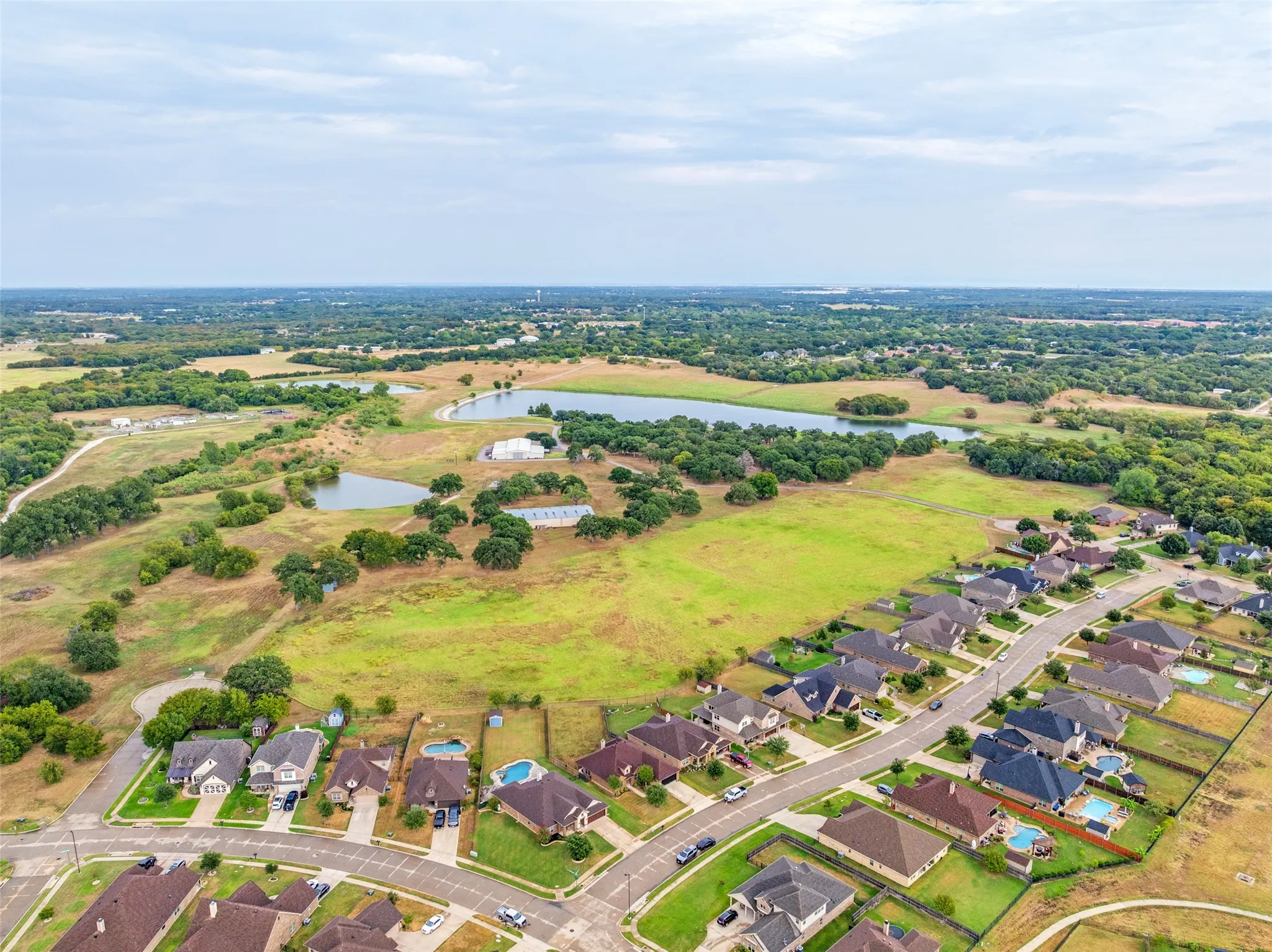 Aerial perspective featuring a residential street, multiple properties with fenced backyards, and expansive green spaces