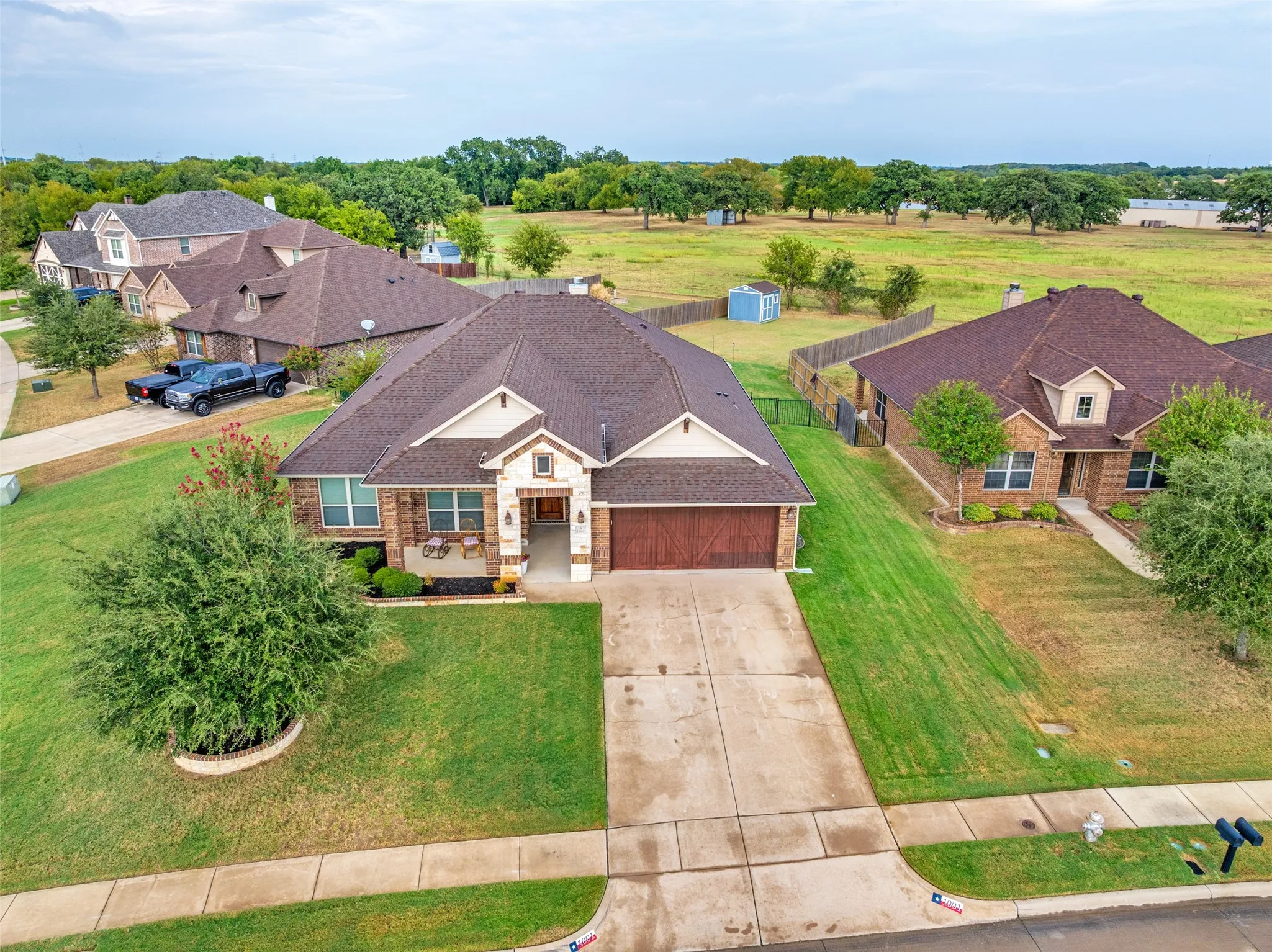 Brick exterior with stone accents, attached two-car garage, concrete driveway, front yard landscaping, and a fenced backyard