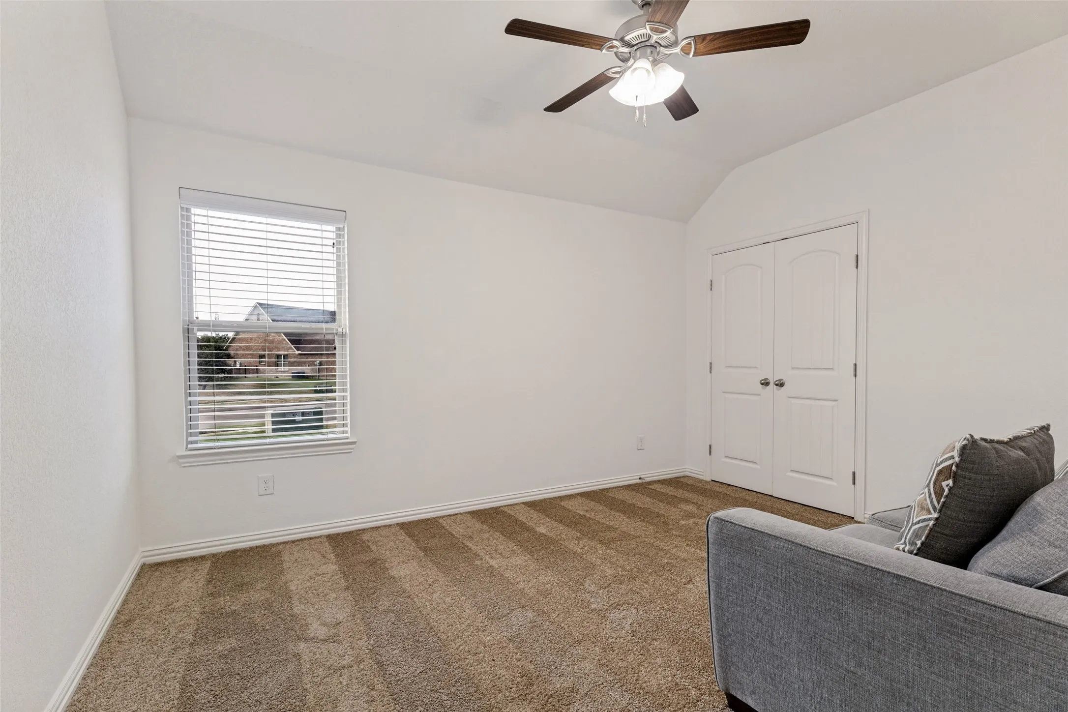 Vaulted ceiling with a ceiling fan, white paneled walls, window with blinds, and white bi-fold closet doors