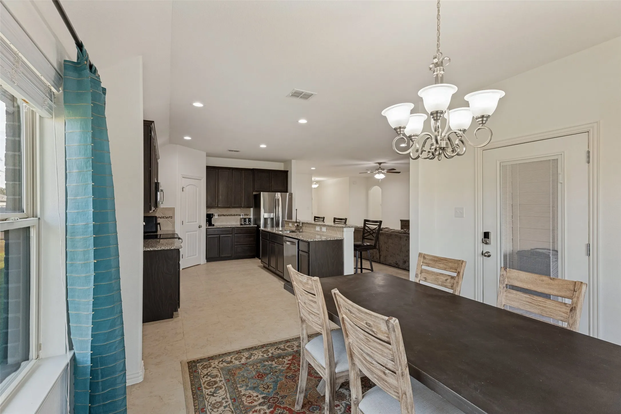 Open-concept kitchen and dining area featuring dark wood-finish cabinetry, stainless steel appliances, and light-toned tile flooring