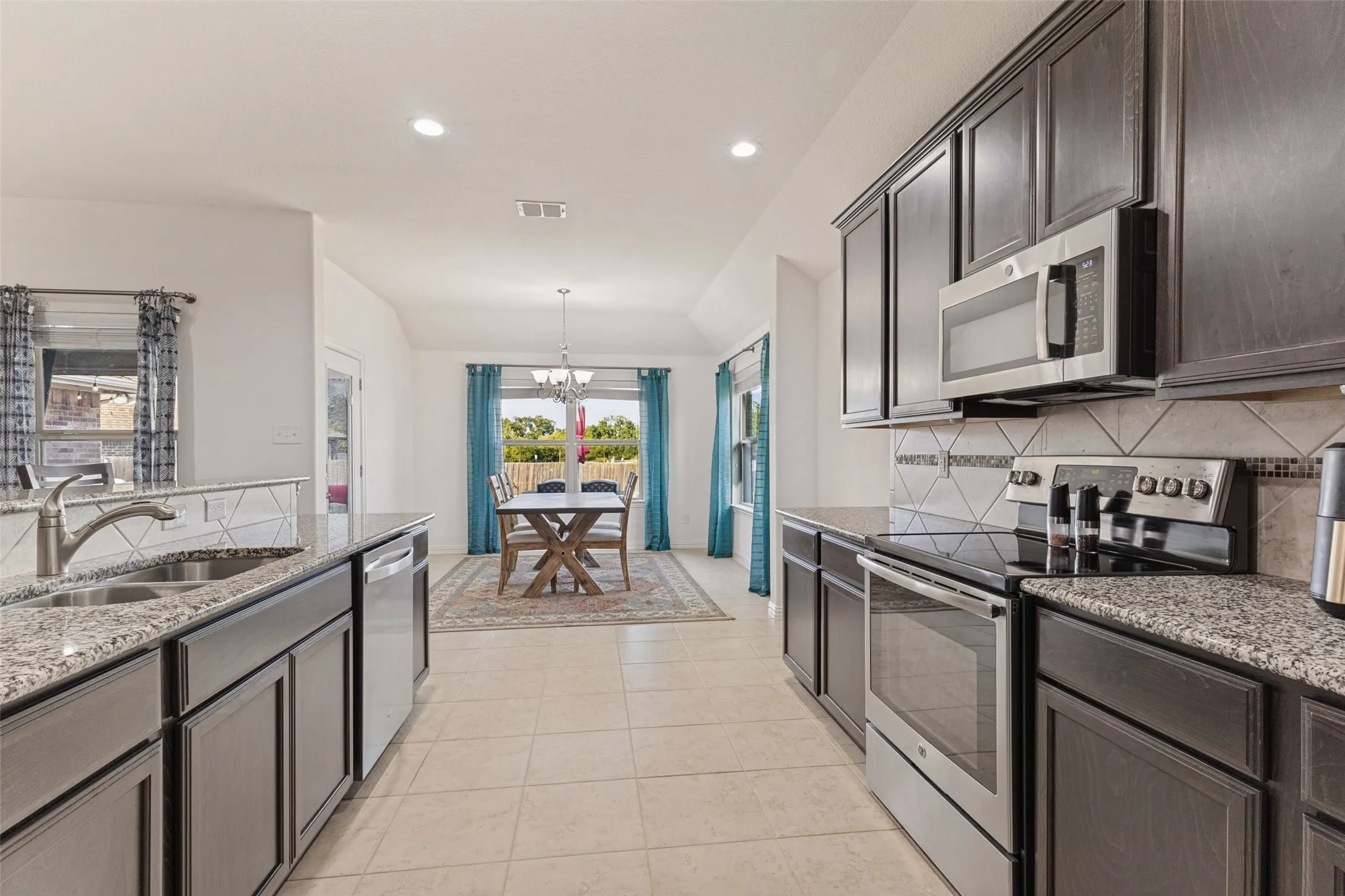 Kitchen featuring dark wood-finish cabinetry, granite countertops, tile flooring, and stainless steel appliances