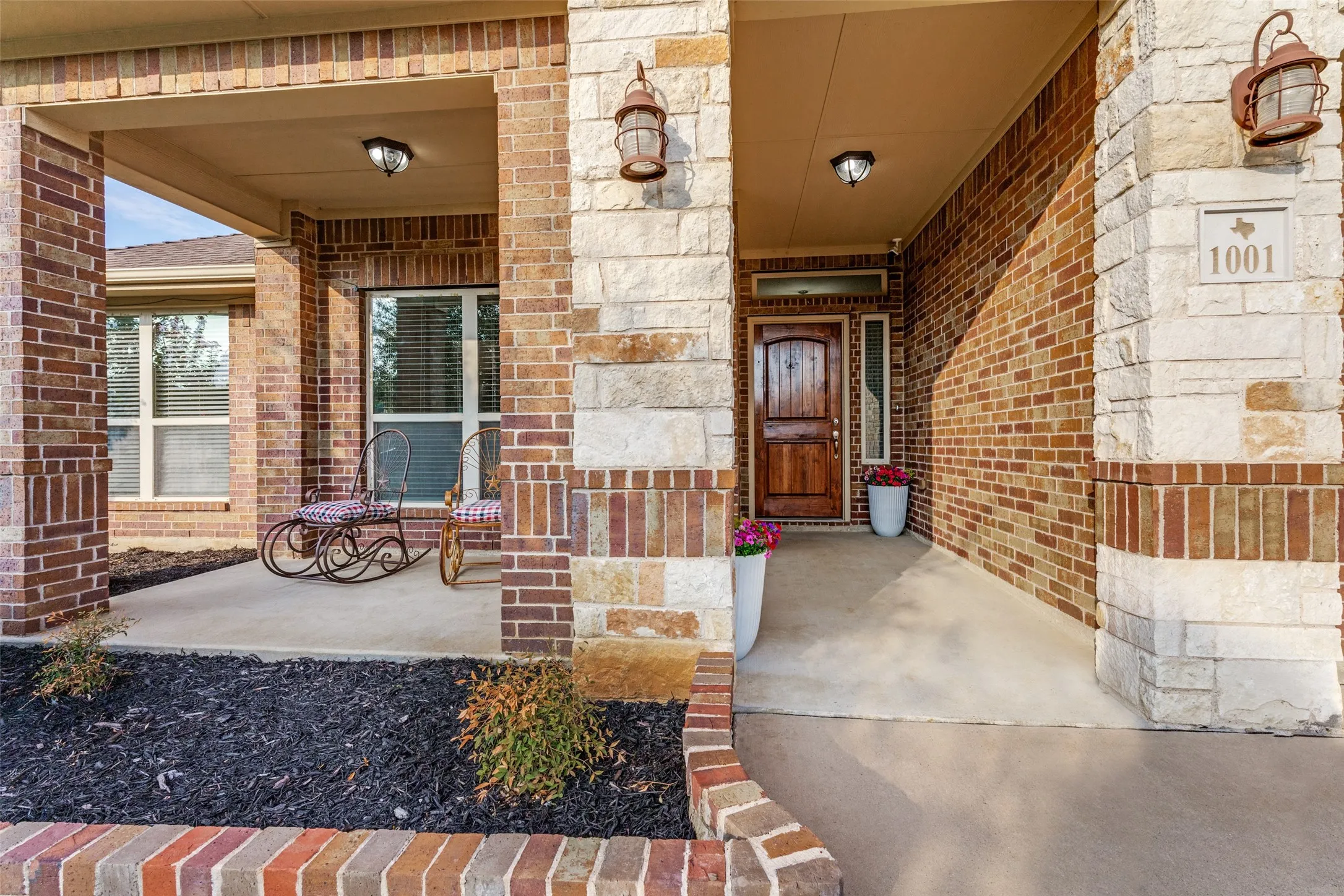 Brick and stone facade featuring a covered porch, solid wood entry door, and exterior sconce lighting