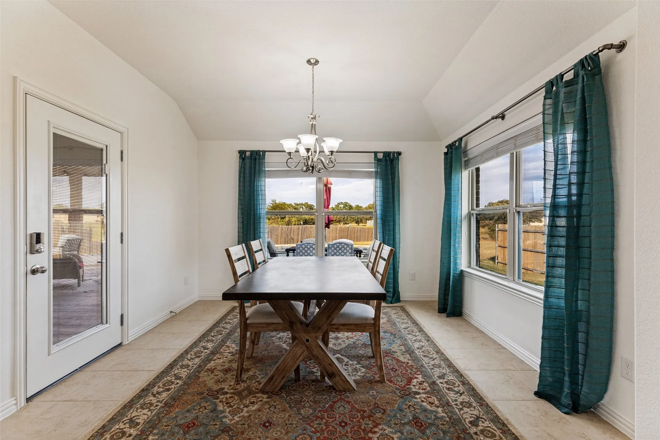 Vaulted ceiling with a chandelier, tile flooring, and multiple windows