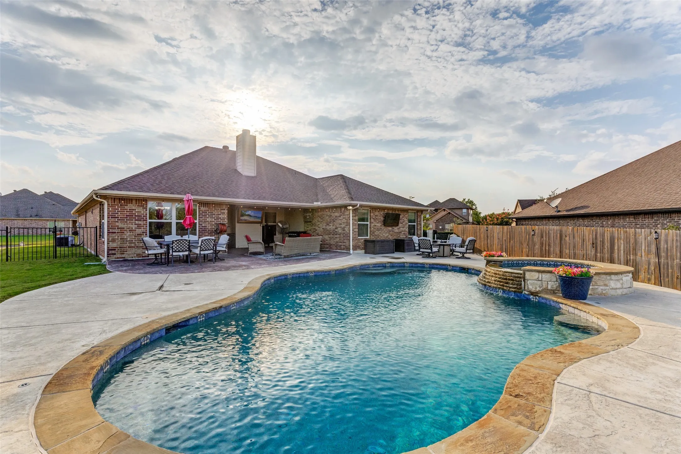 Freeform swimming pool with integrated spa and waterfall feature, expansive concrete patio, and brick exterior