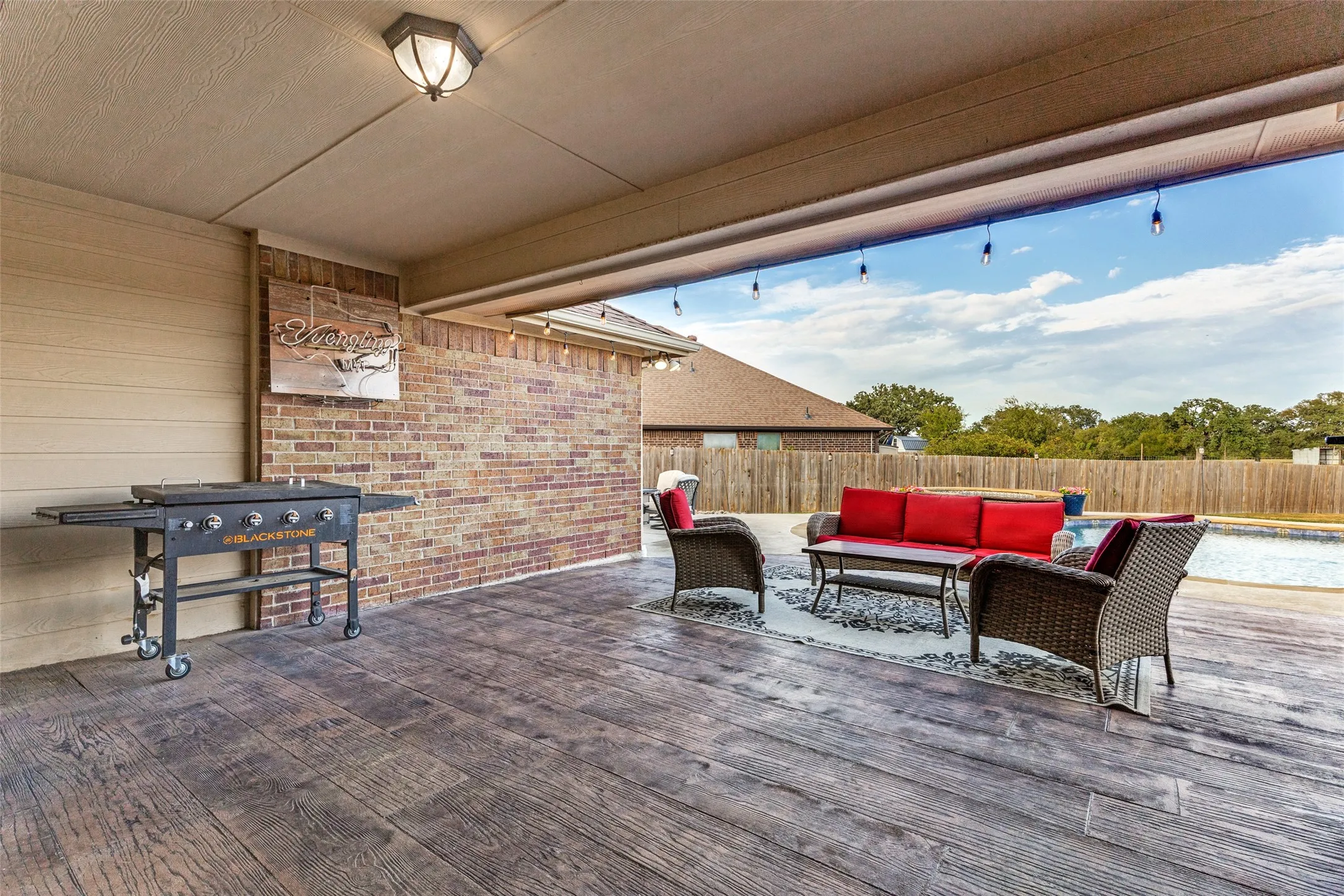 Covered patio featuring wood-finish flooring, brick accent wall, and string lighting