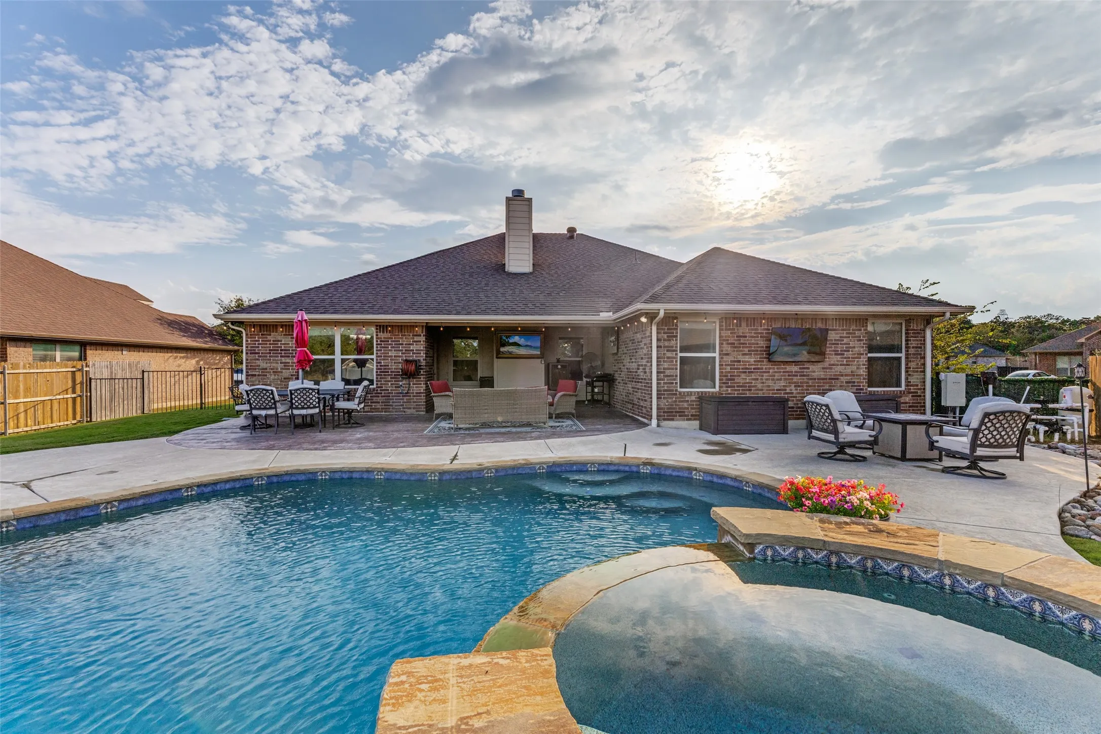 Swimming pool with an integrated spa, extensive concrete patio, exterior brick finish, and a shingle roof