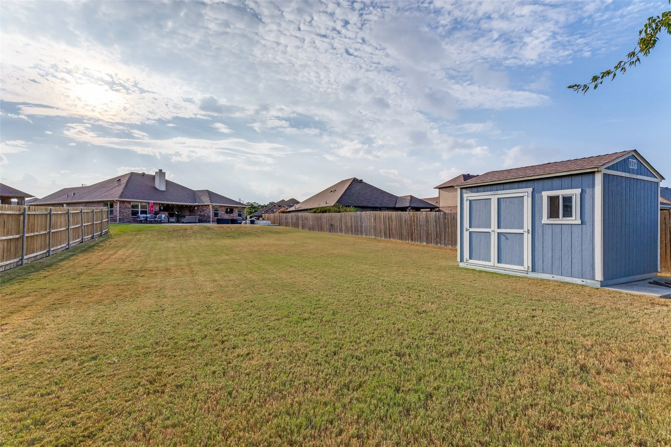 Expansive backyard featuring a manicured lawn, a blue storage shed, and a wooden privacy fence