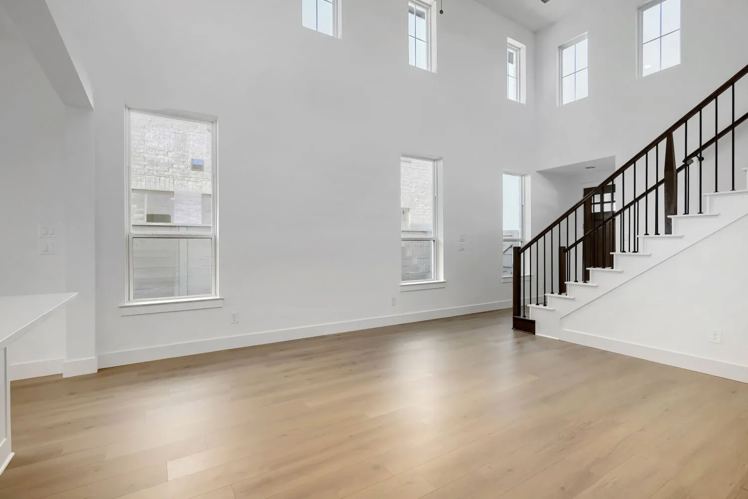 High ceilings with multiple windows, wood-finish flooring, and a staircase featuring dark wood handrails and black balusters