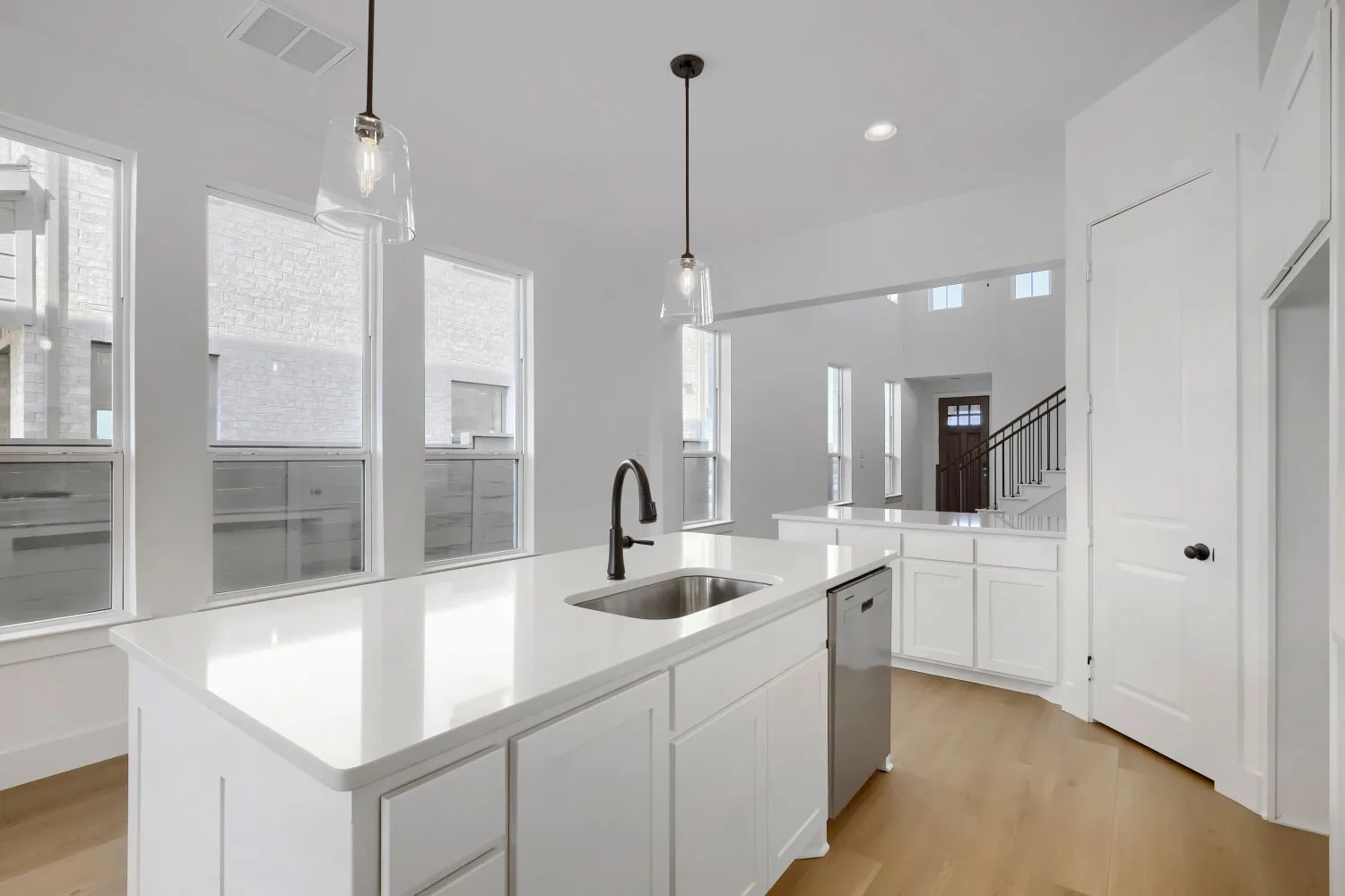 Kitchen island with a built-in sink, white cabinetry, integrated dishwasher, and light-toned wood-finish flooring