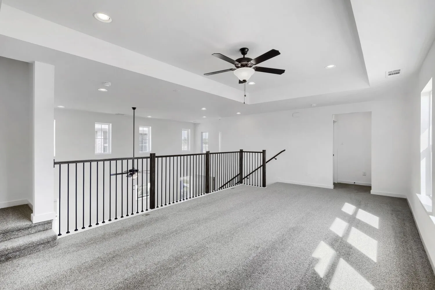 Spacious upper-level area with neutral carpeting, recessed lighting, ceiling fan, and white walls