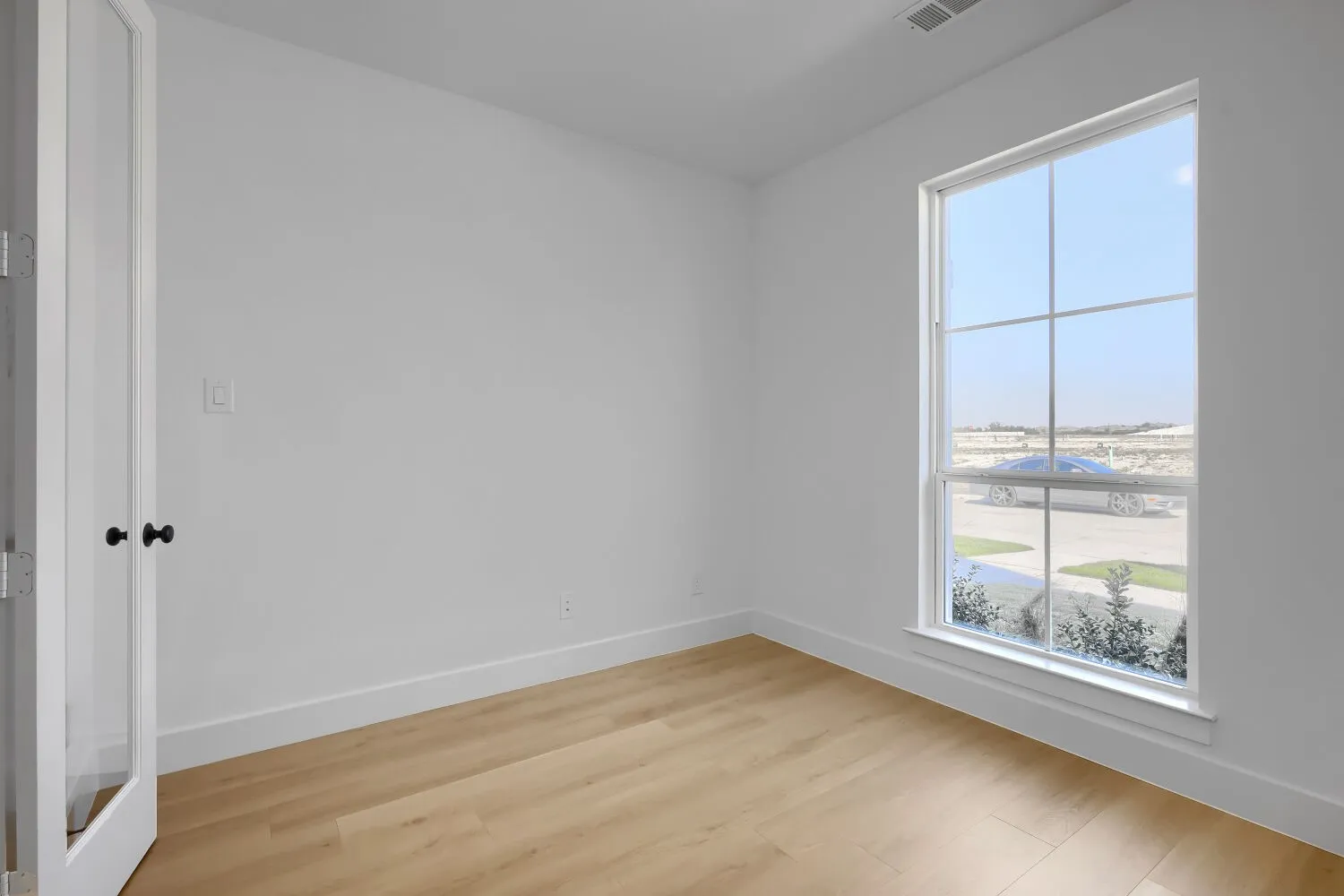 Bright corner bedroom featuring expansive windows with grid-pane detailing, abundant natural light, and warm wood-finish flooring throughout