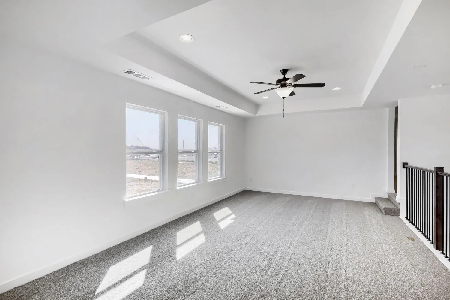 Recessed lighting, ceiling fan, white tray ceiling, three windows, and carpet flooring
