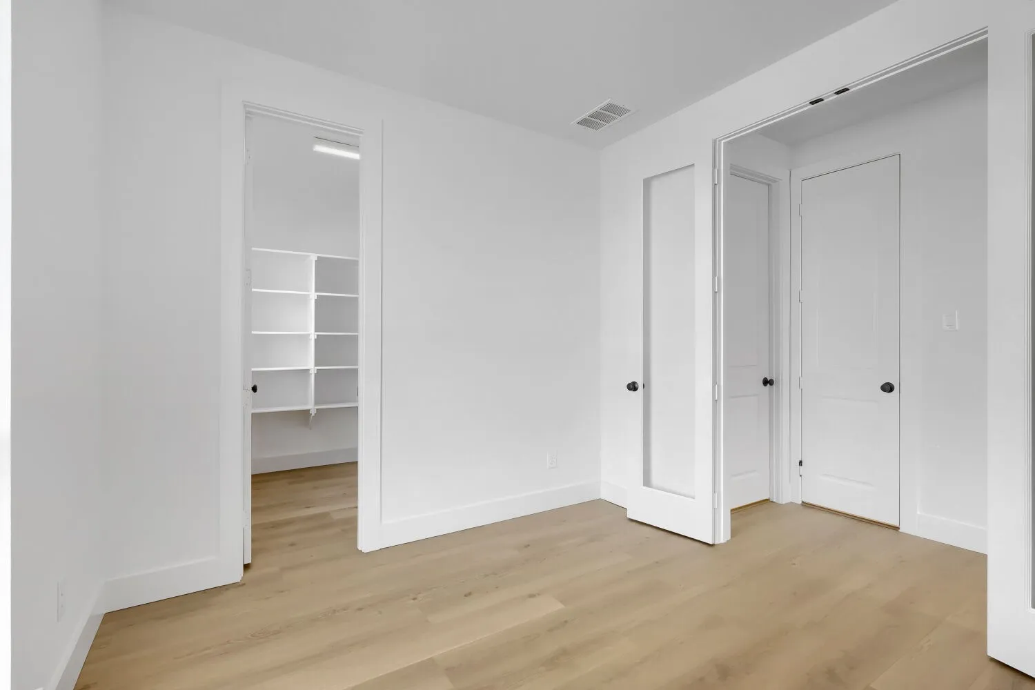 Neutral wall paint, wood-finish flooring, white trim, and multiple interior doors
