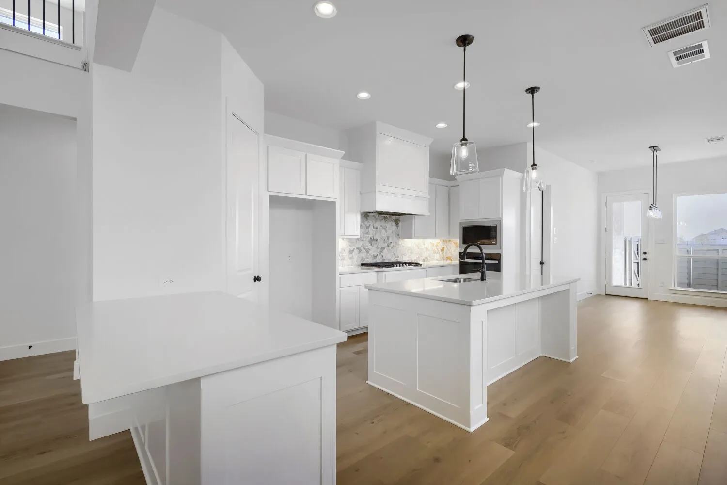 Modern kitchen featuring white cabinetry, a large center island with waterfall countertop, stainless steel appliances, marble subway tile backsplash, pendant lighting, and wide-plank wood-finish flooring throughout the open-concept living area