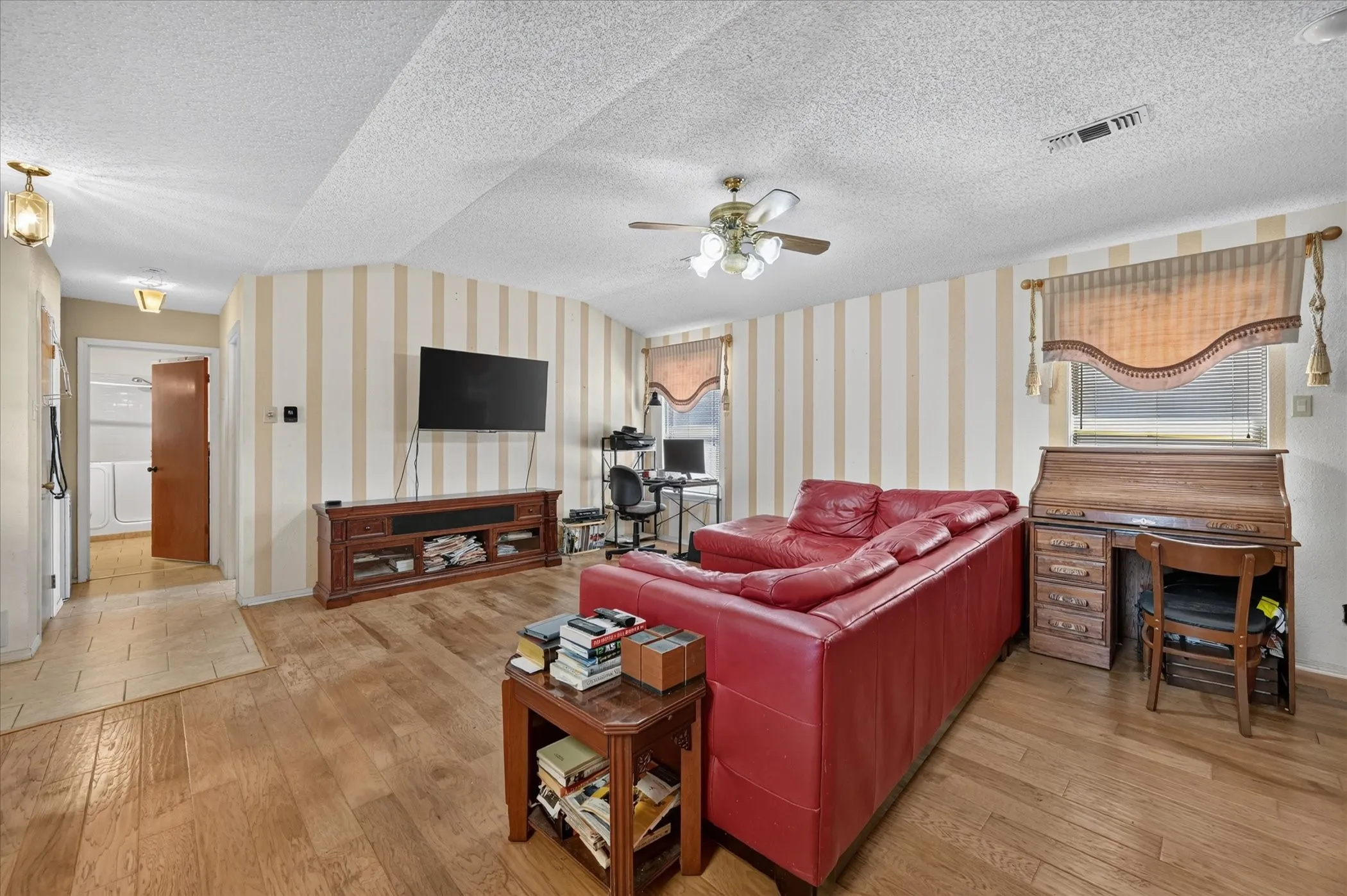 Wood-finish flooring, ceiling fan, curved wall detail, recessed lighting, and a built-in media console