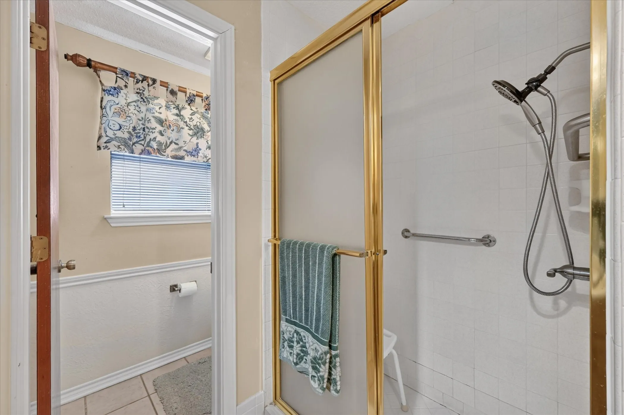 Shower enclosure with gold-finish framing, white tile surround, and a handheld shower fixture