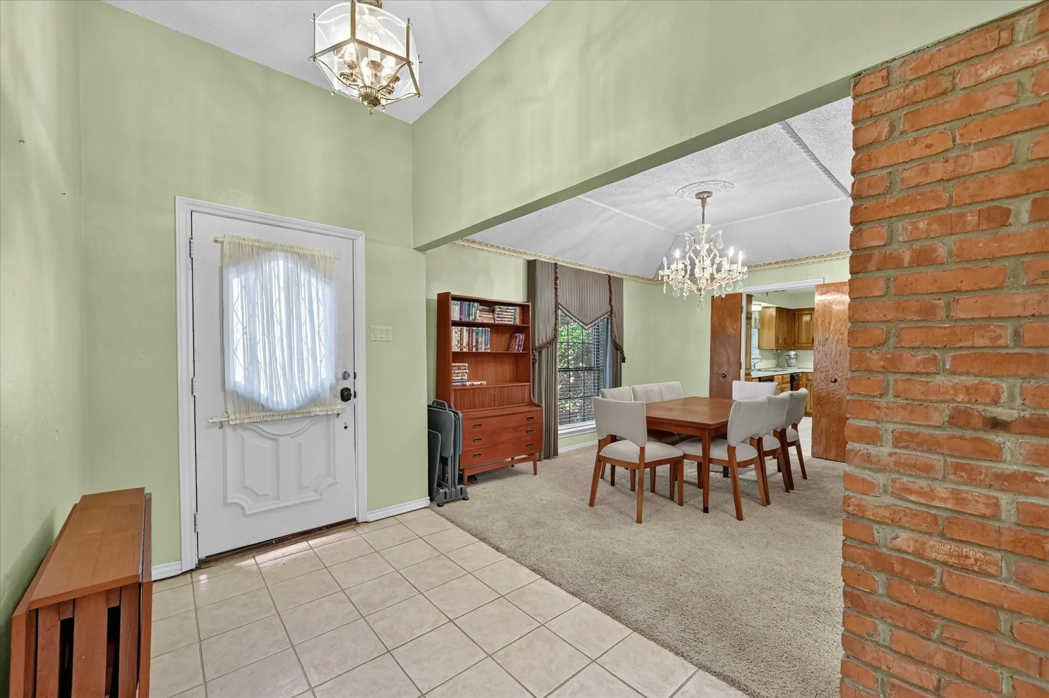 Entry foyer with tile flooring and a vaulted ceiling, opening to a carpeted dining area featuring a chandelier