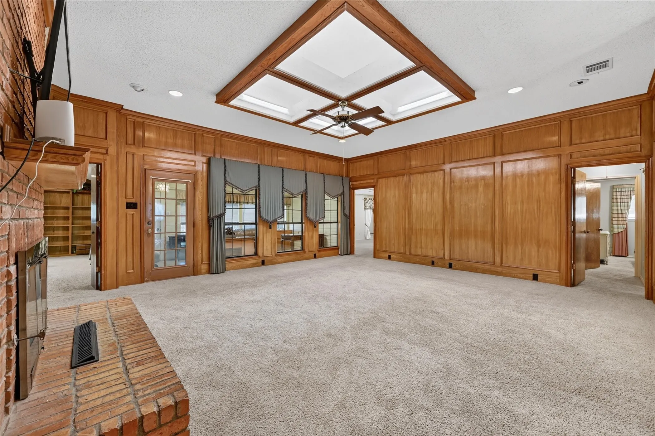 Expansive room featuring wood paneling, a brick fireplace, built-in shelving, and a tray ceiling with a fan