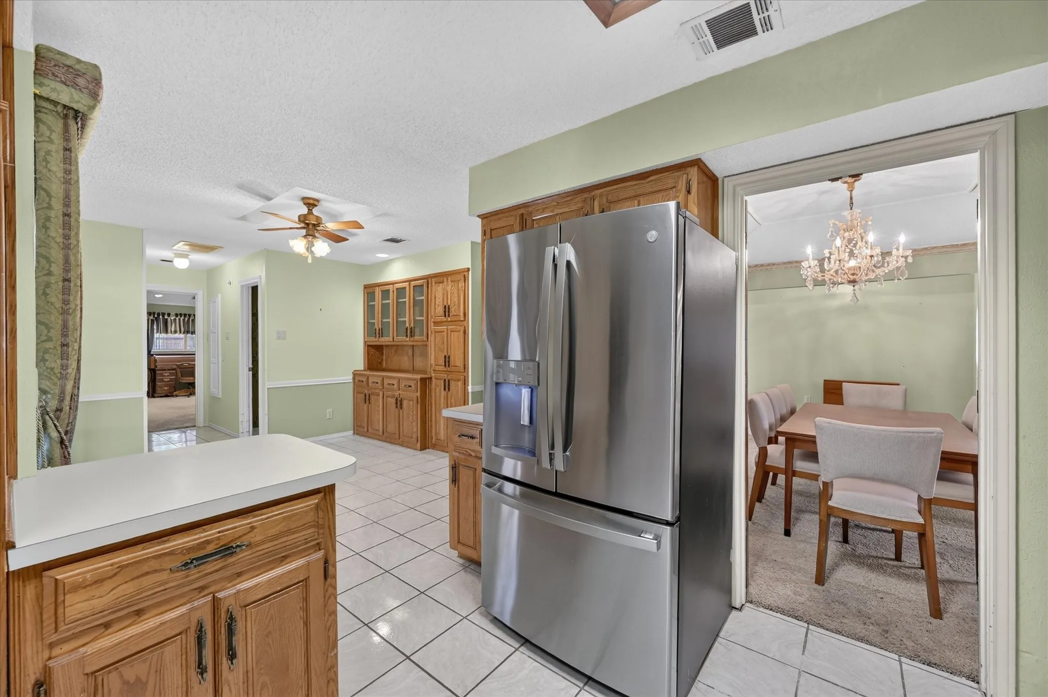 Kitchen featuring tile flooring, wood cabinetry, a built-in hutch with glass-front uppers, a stainless steel refrigerator, and ceiling fans